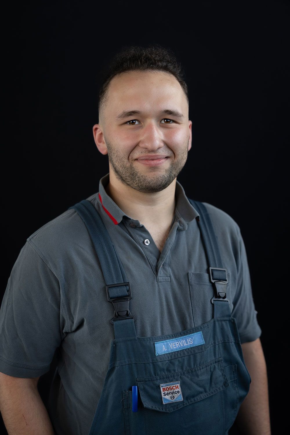 Ein Mann in Overalls und grauem Hemd lächelt in die Kamera.