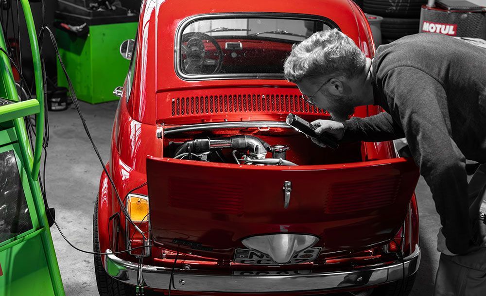 Ein Mann arbeitet in einer Garage an einem roten Auto.