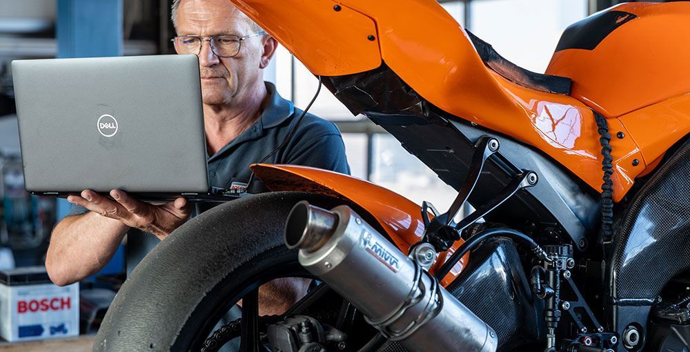 Ein Mann arbeitet an einem Motorrad und benutzt gleichzeitig einen Laptop.