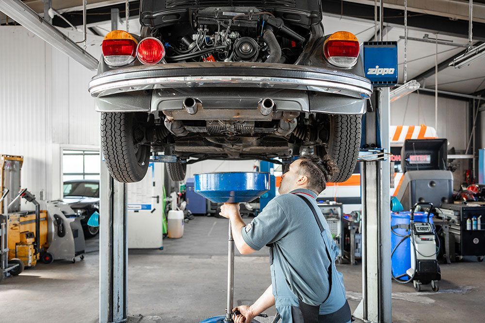Ein Mann arbeitet auf einer Hebebühne in einer Garage an einem Auto.