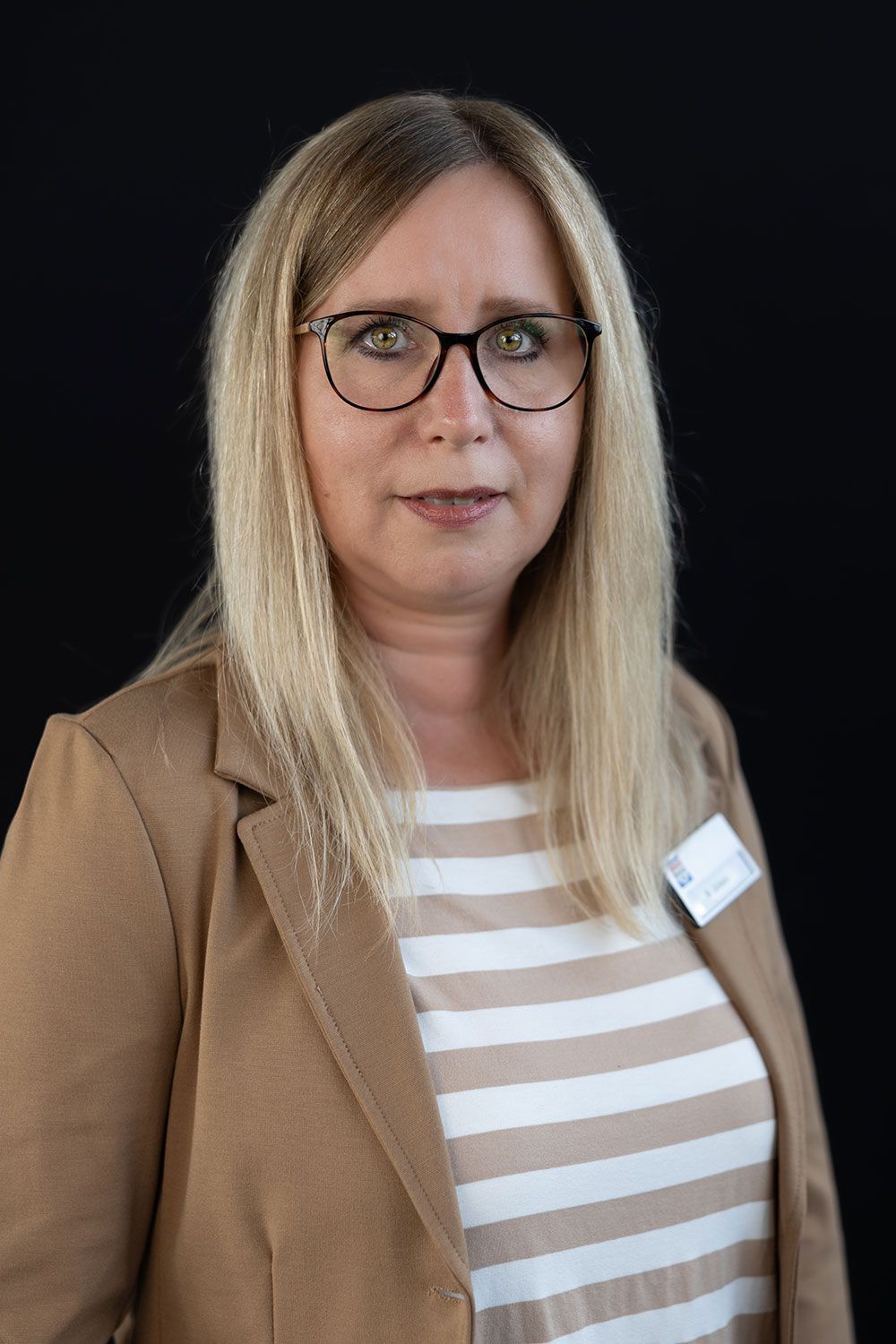 Eine Frau mit Brille und gestreiftem Hemd steht vor einem schwarzen Hintergrund.