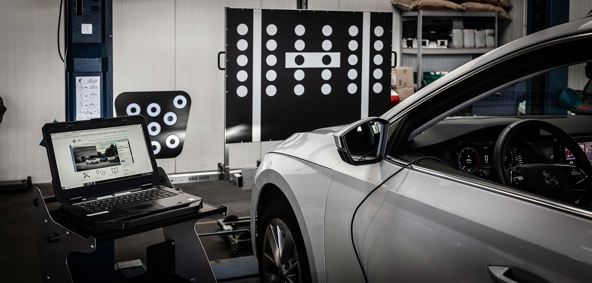 In einer Garage steht ein Auto neben einem Laptop.