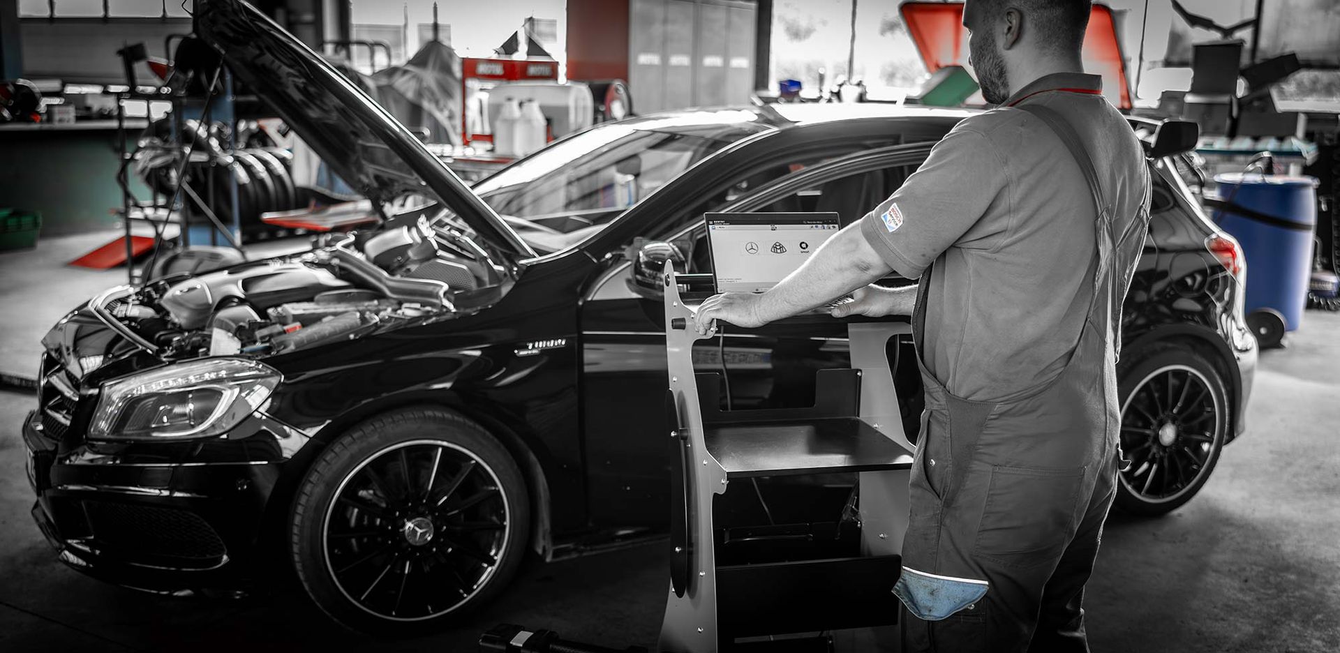 Ein Mann arbeitet in einer Garage mit geöffneter Motorhaube an einem Auto.