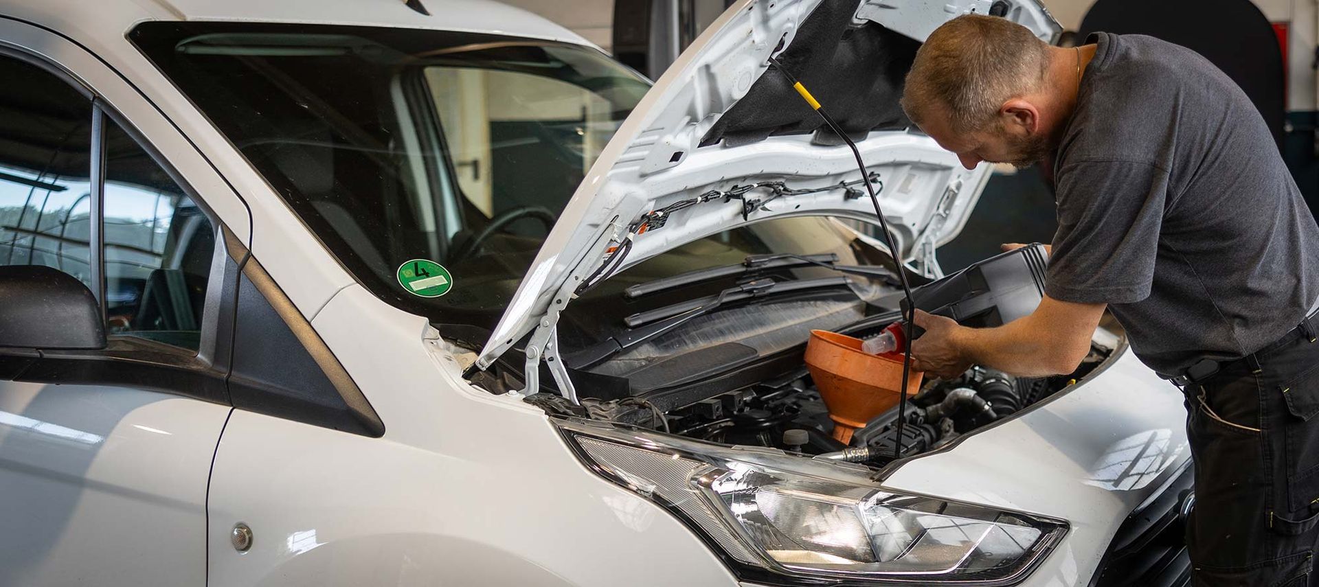 Ein Mann arbeitet am Motor eines weißen Lieferwagens.