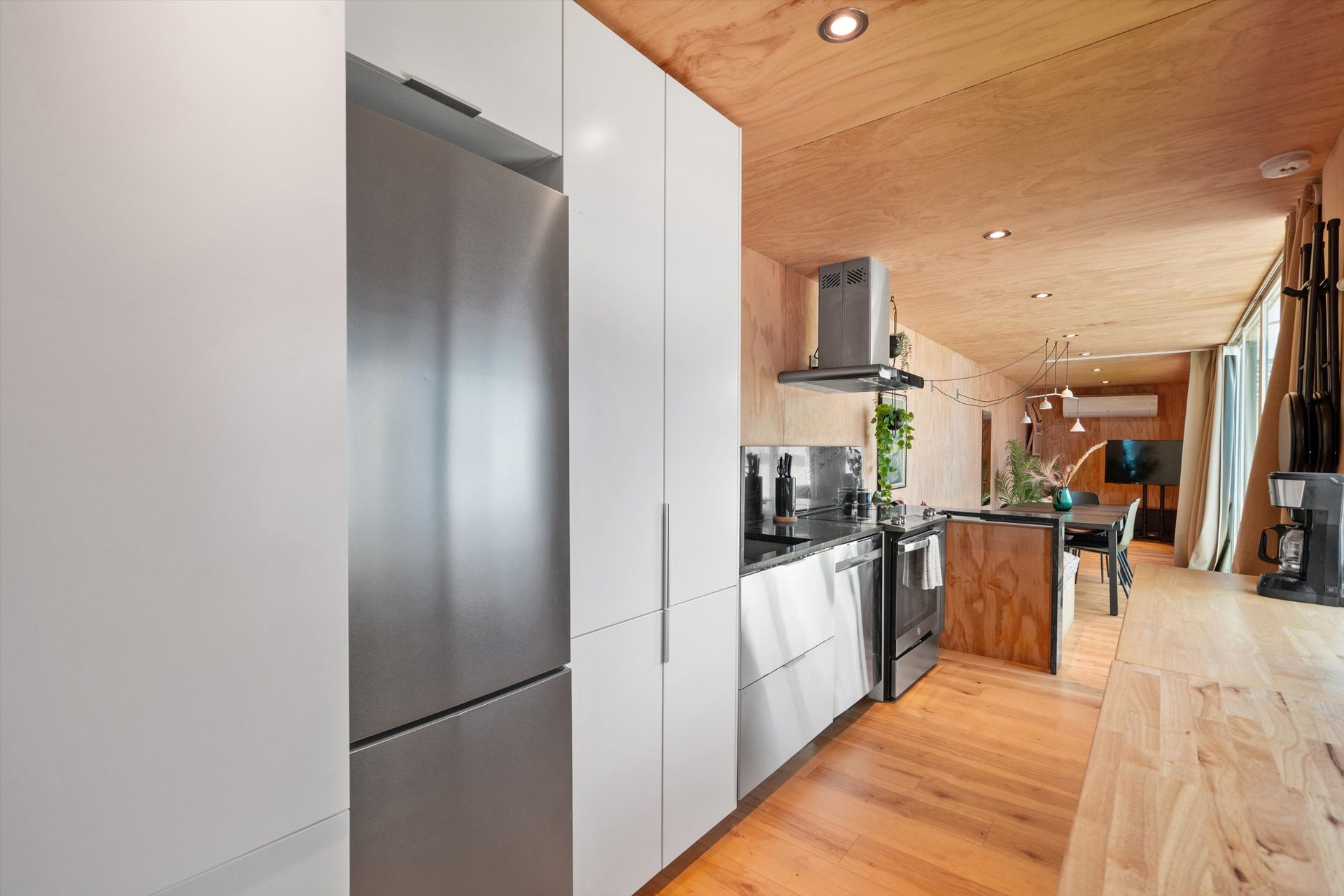 Modern kitchen with white cabinets, stainless steel appliances, and a wood-paneled ceiling and floor.