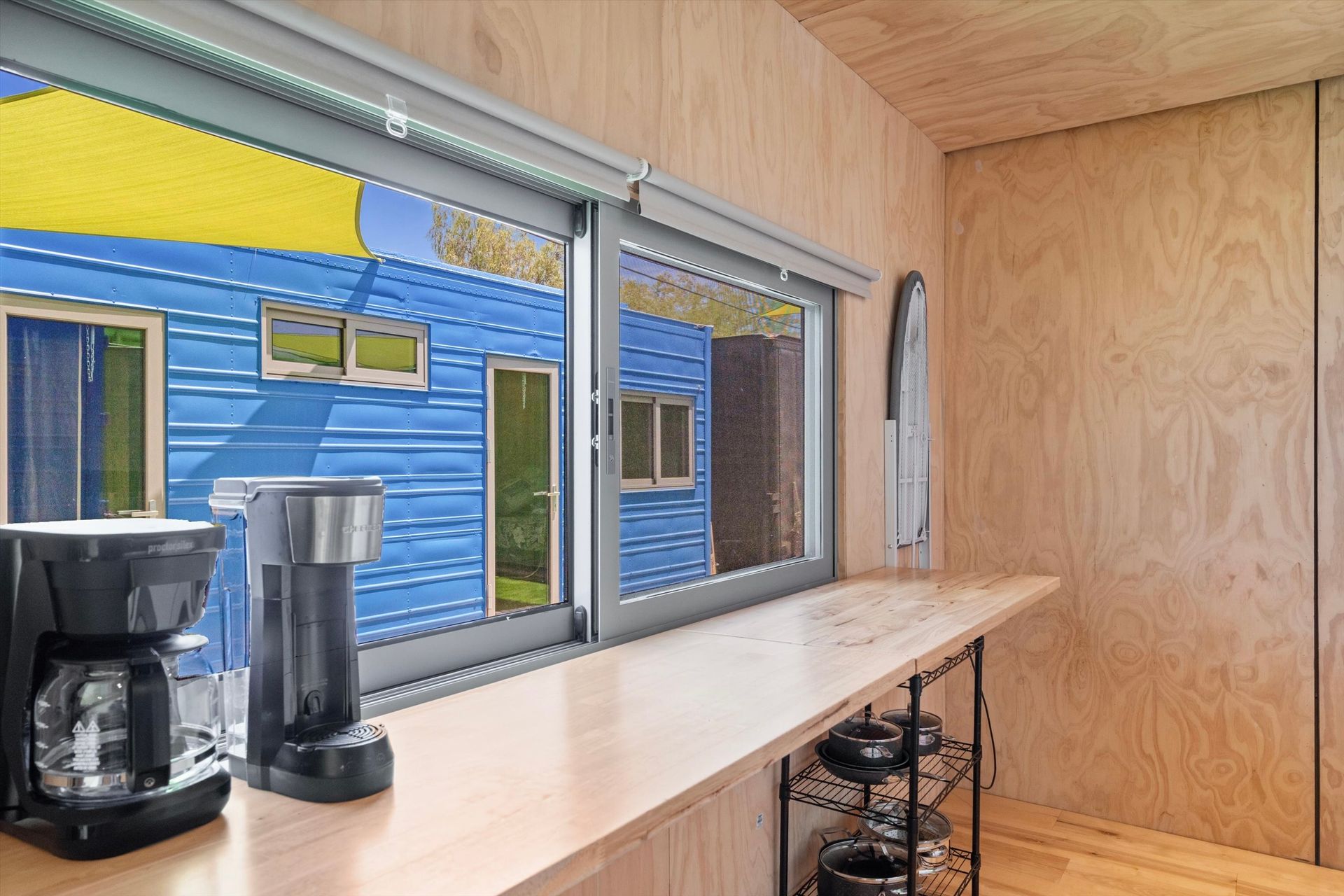 Interior view of a small room with a window overlooking a blue building.  A coffee maker sits on the countertop.