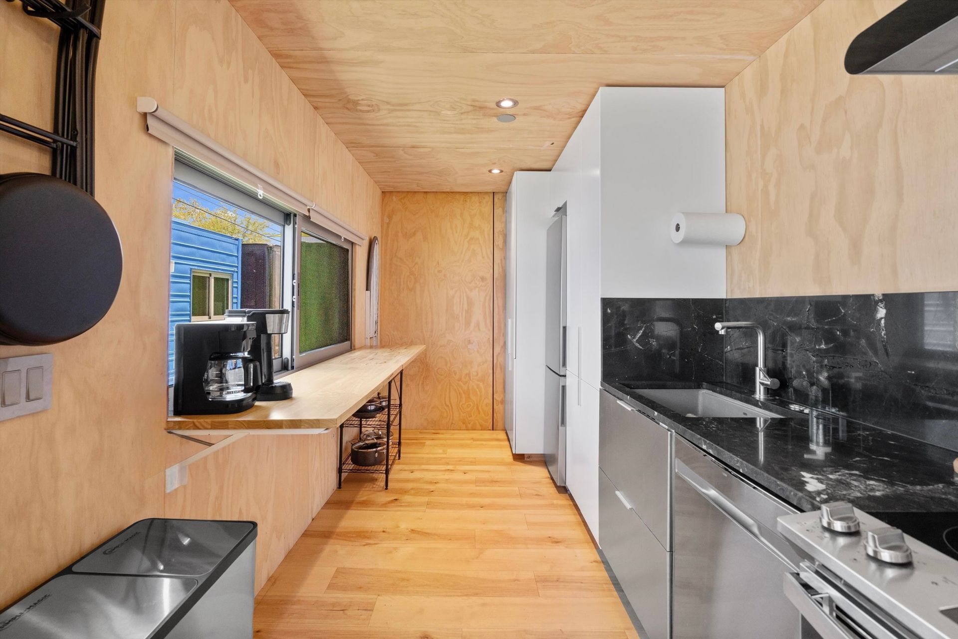 Interior of a modern kitchen and dining area. Light wood paneling covers the walls and ceiling, with a stainless steel kitchen and countertop.