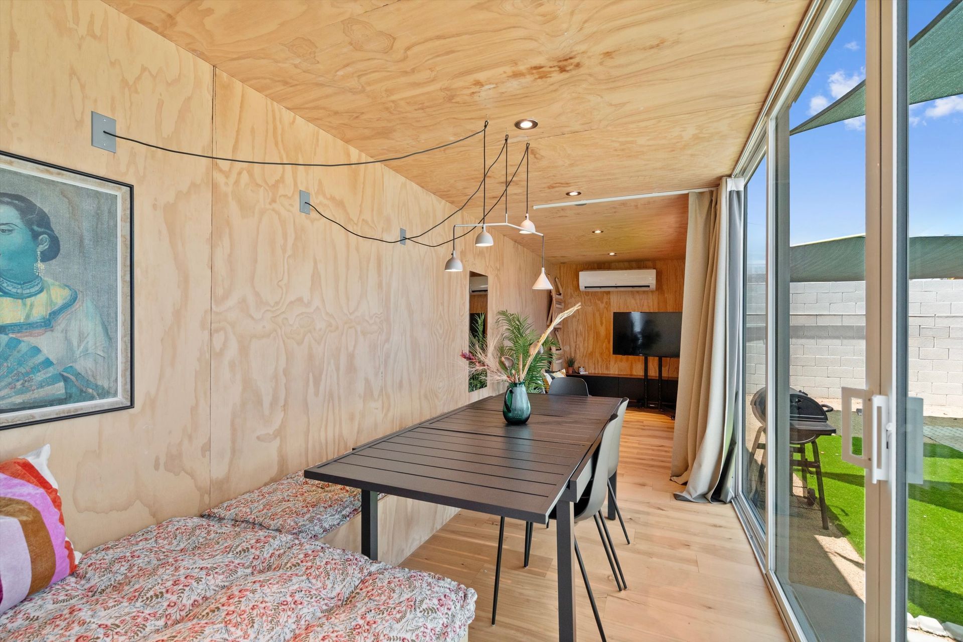 Dining area with wooden walls, a black table, and sliding glass doors leading to a grassy area. A painting and decorative lighting are also present.