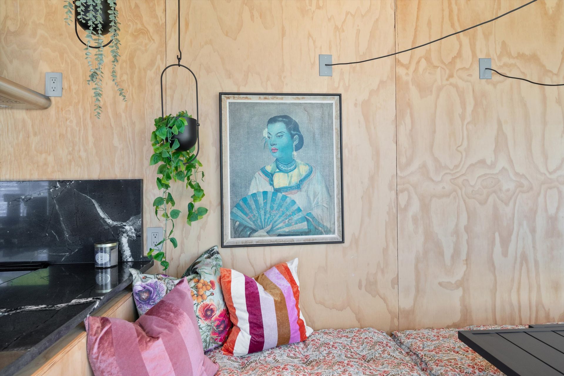 Cozy corner with wood paneling, art, pillows, and hanging plant, and a marble countertop.