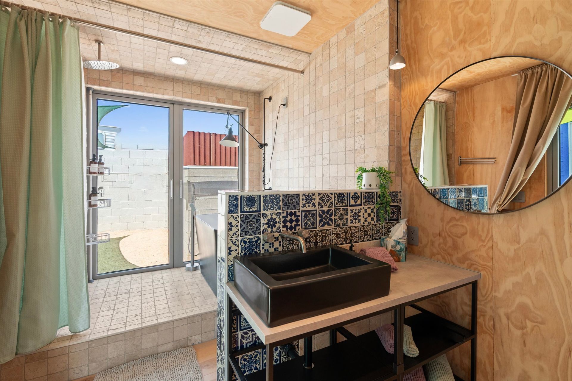 Bathroom with wood paneling, black sink, patterned backsplash, and large window with outdoor view. Round mirror on the wall.