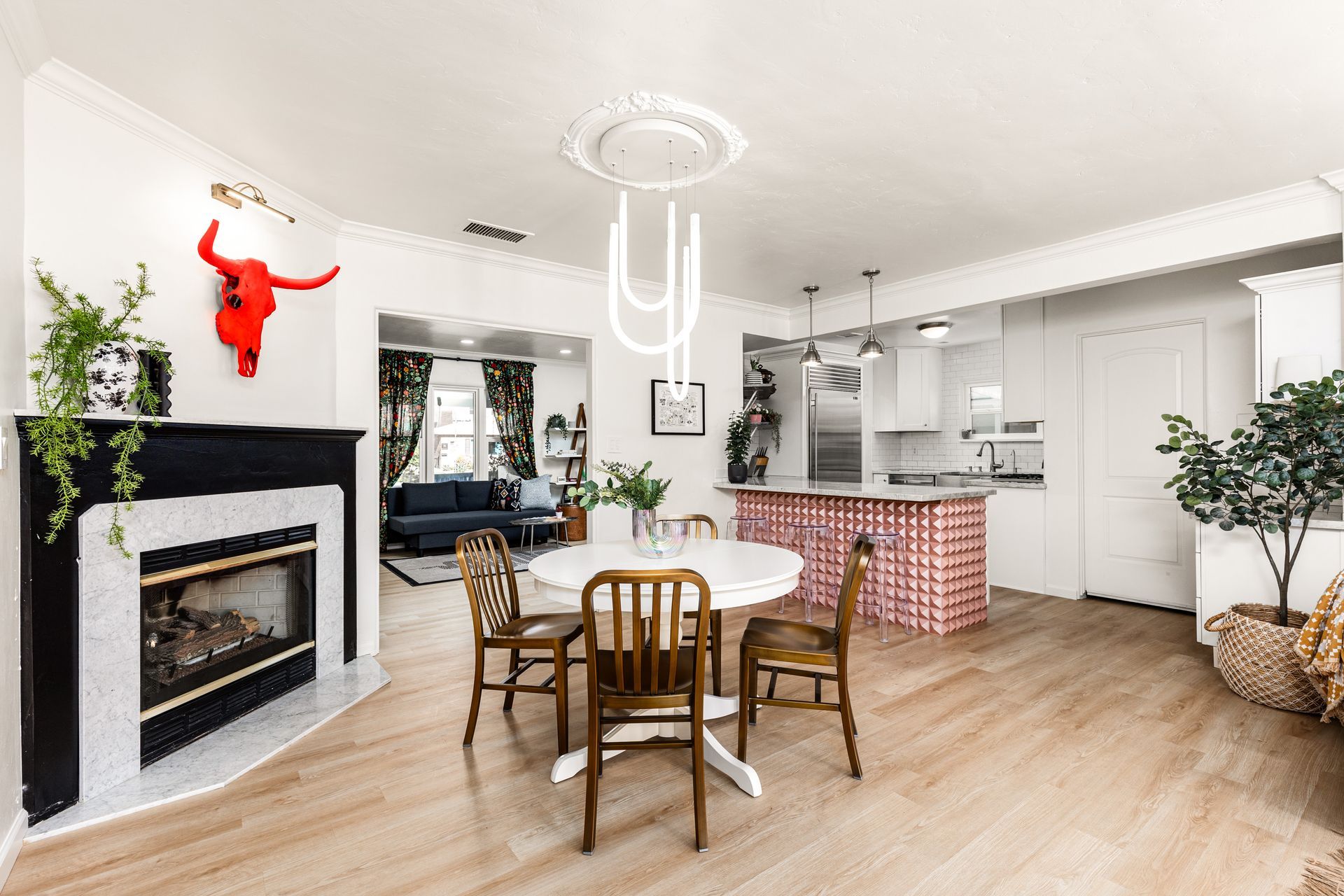 A bright open-plan living space with a fireplace, dining area, and kitchen. White walls, light wood floors, and colorful accents create a vibrant interior.