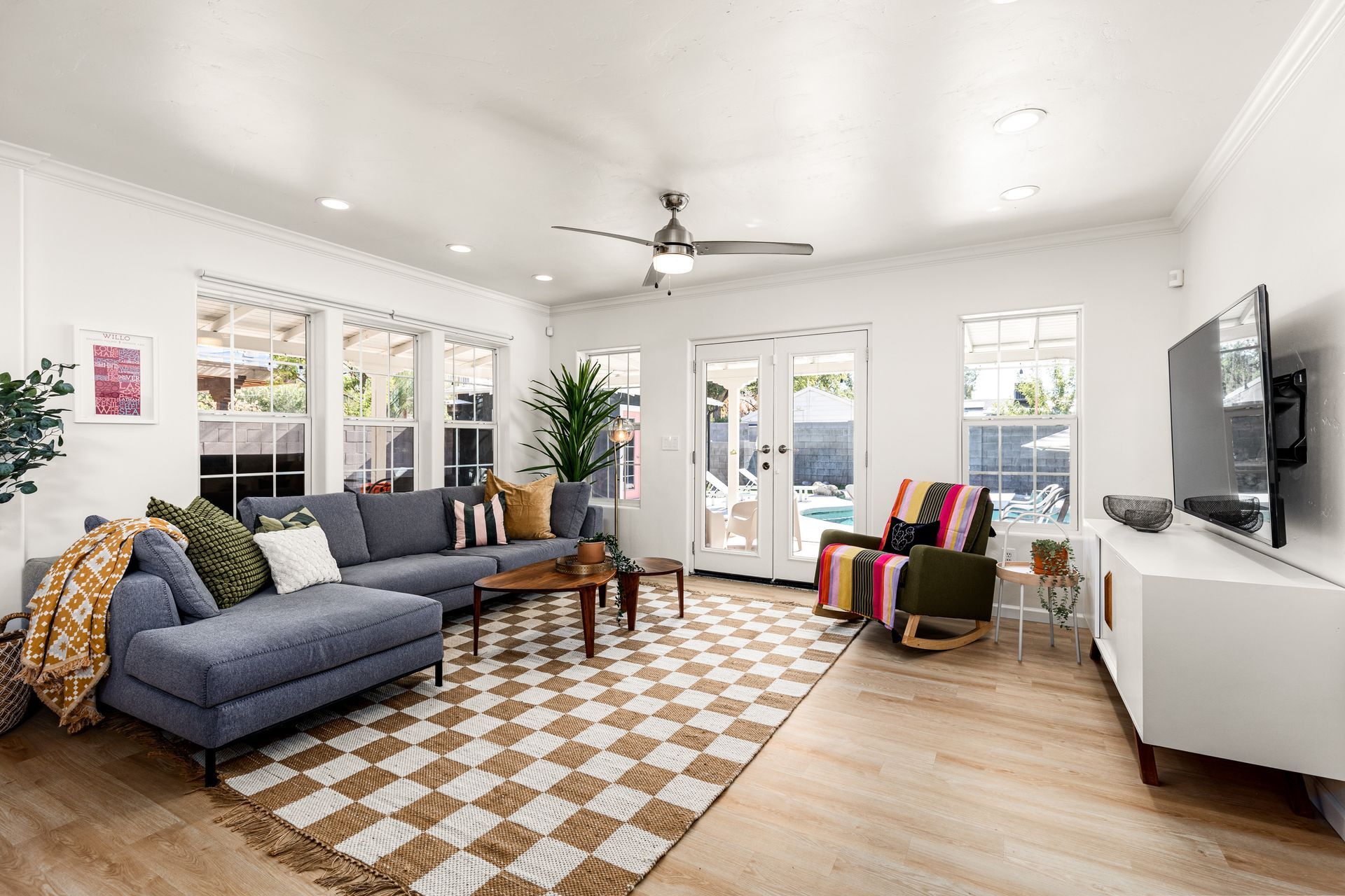 Spacious living room with blue sectional sofa, patterned rug, white walls, and a view of a pool through french doors.