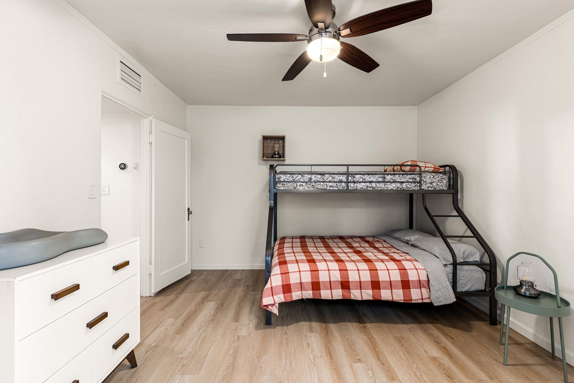 A bedroom with a bunk bed, dresser, and a small chair.  Light wooden floors and white walls.