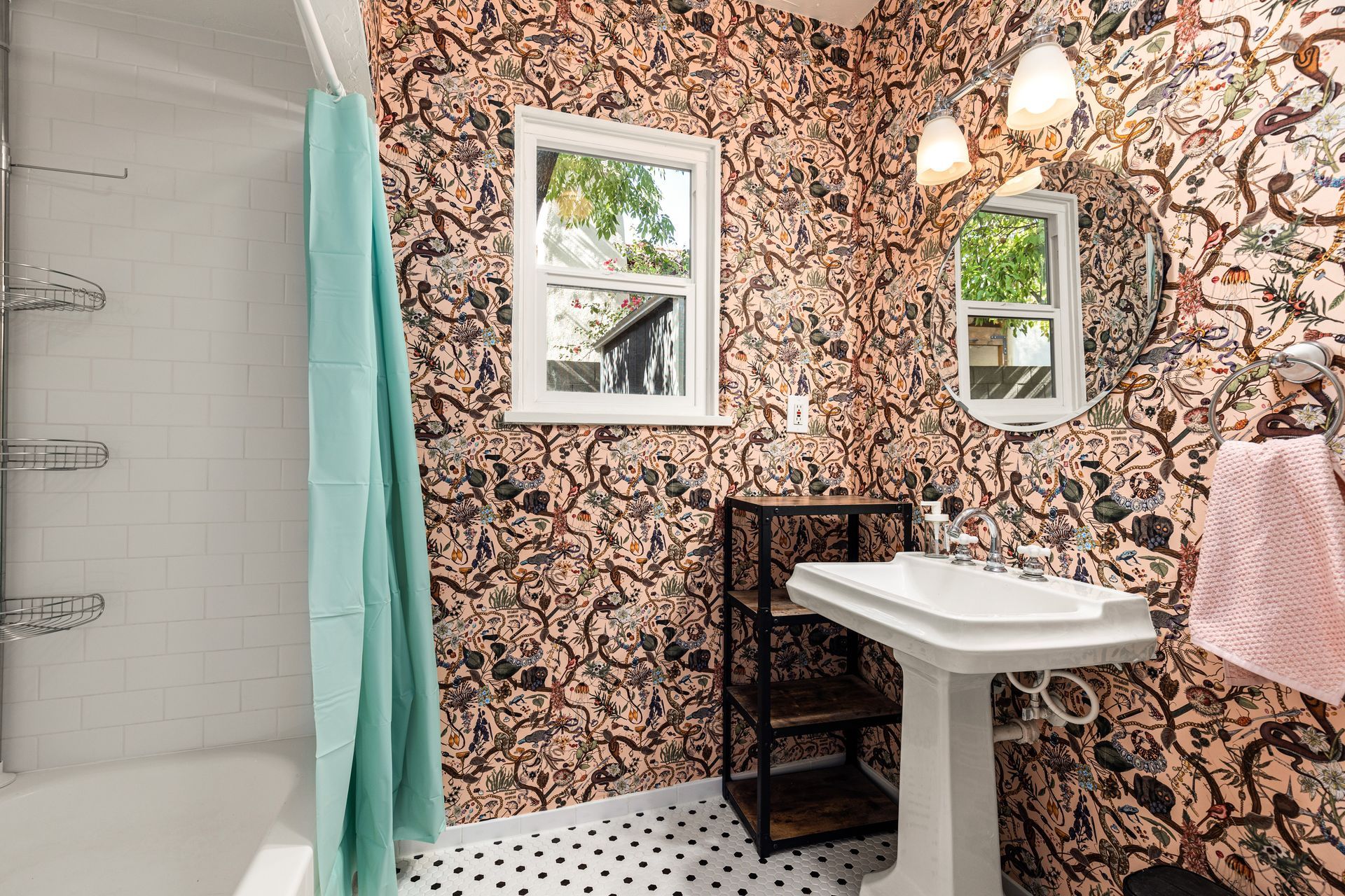 Bathroom with patterned wallpaper, white pedestal sink, and turquoise shower curtain. A window and a towel rack are also visible.