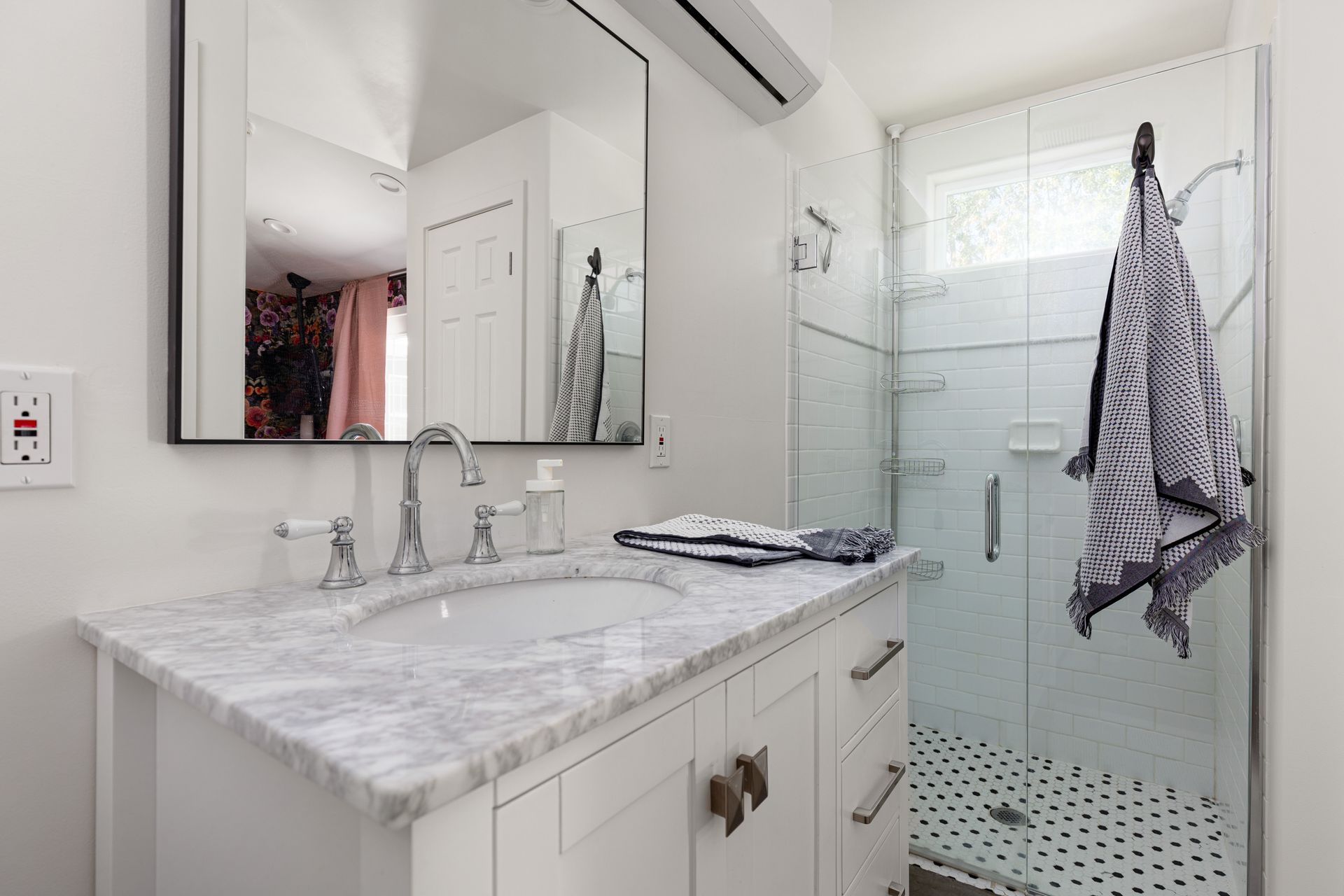 Bathroom with white vanity, marble countertop, large mirror, and glass shower. A towel hangs on the shower door.