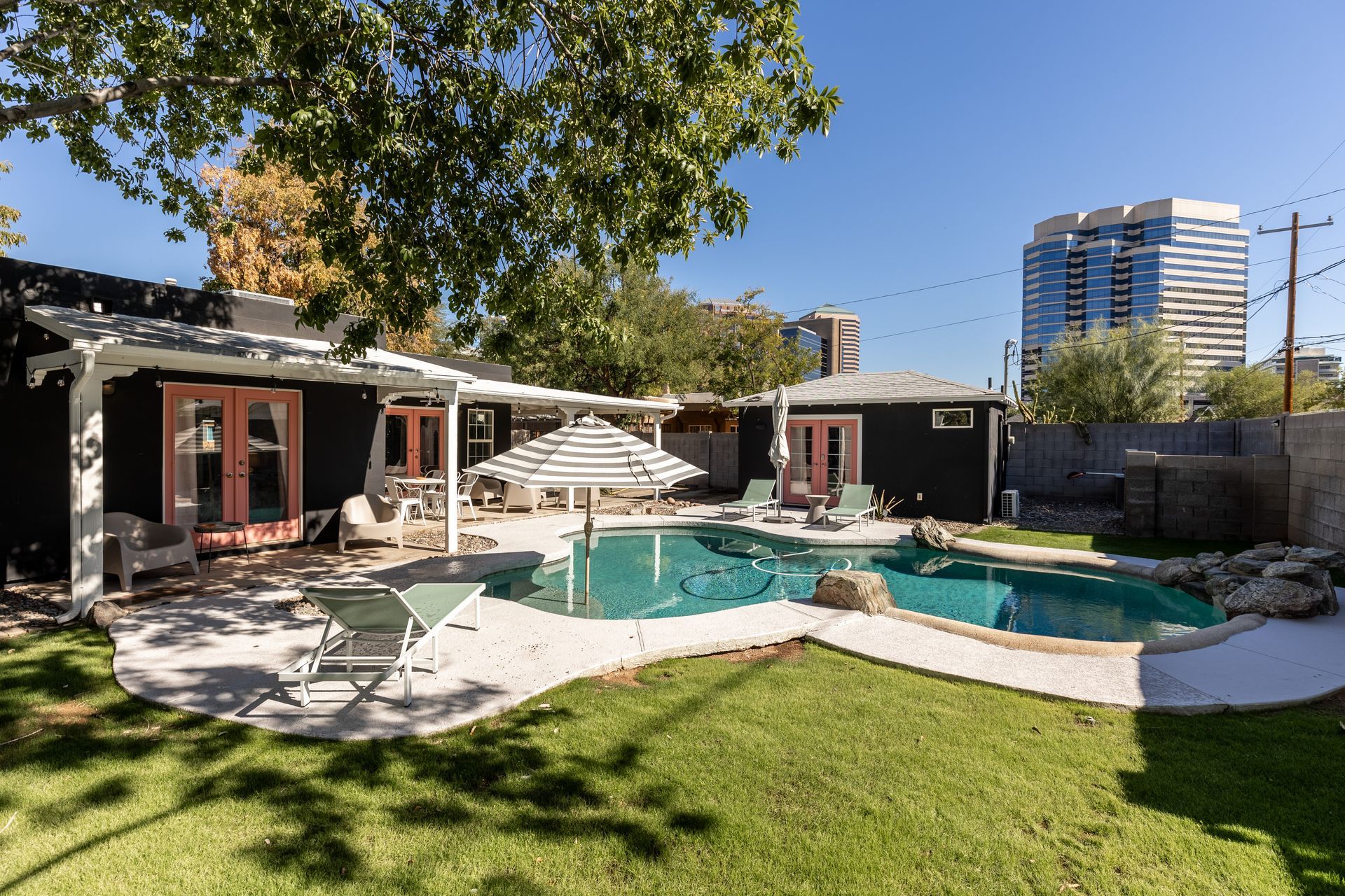 Backyard with a pool, patio, and small black houses. A high-rise building is visible in the background.