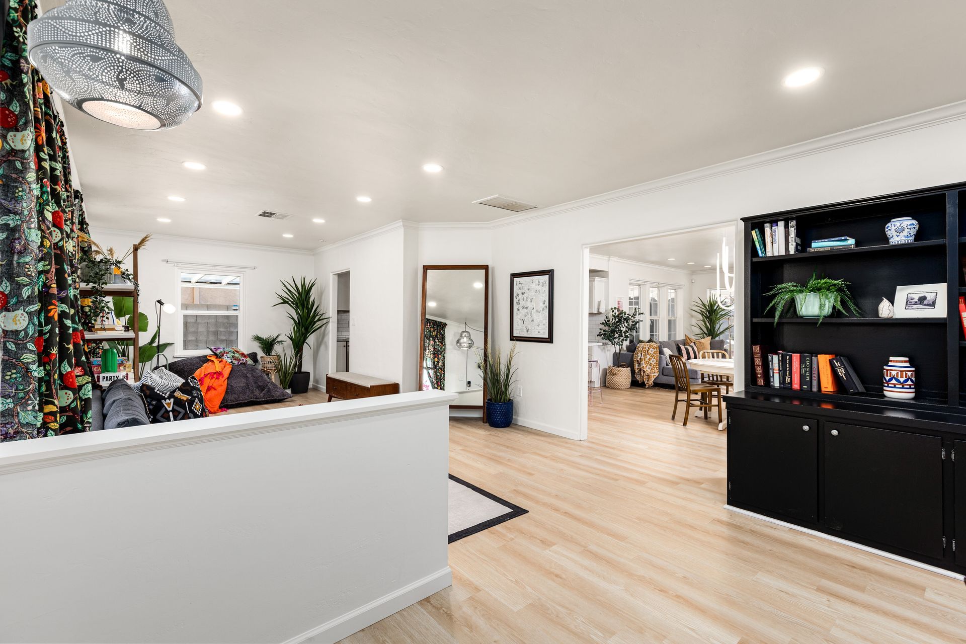 Spacious, bright living area with light wood floors and a black bookcase. There is a mirror and doorway leading to a dining space.