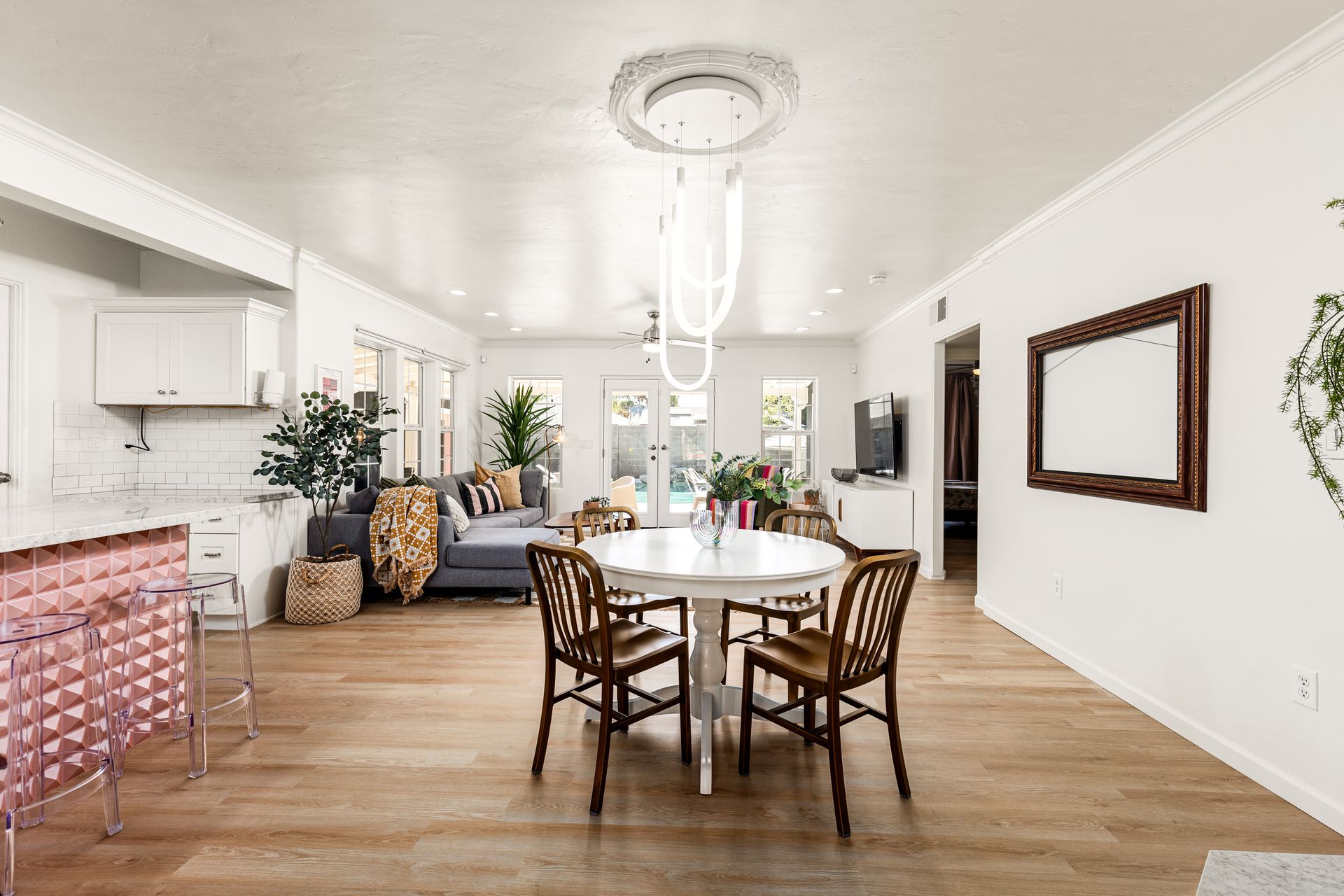 A bright, open-concept dining and living area with white walls, hardwood floors, and a round white table with brown chairs.