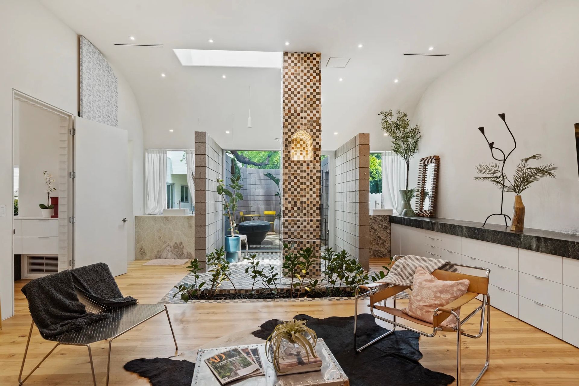 Modern interior with a central water feature, light wood floors, and white walls. Furnishings include armchairs and a coffee table.
