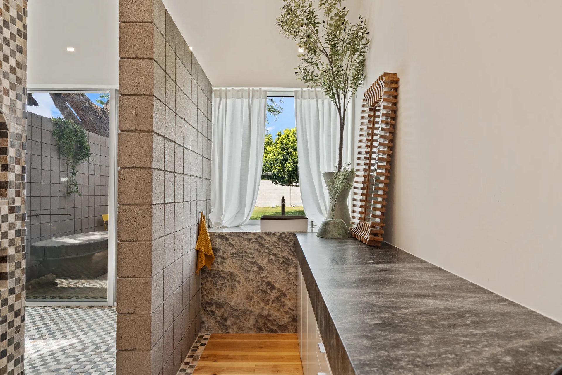 Modern bathroom hallway with stone countertops, neutral walls, and a window view.