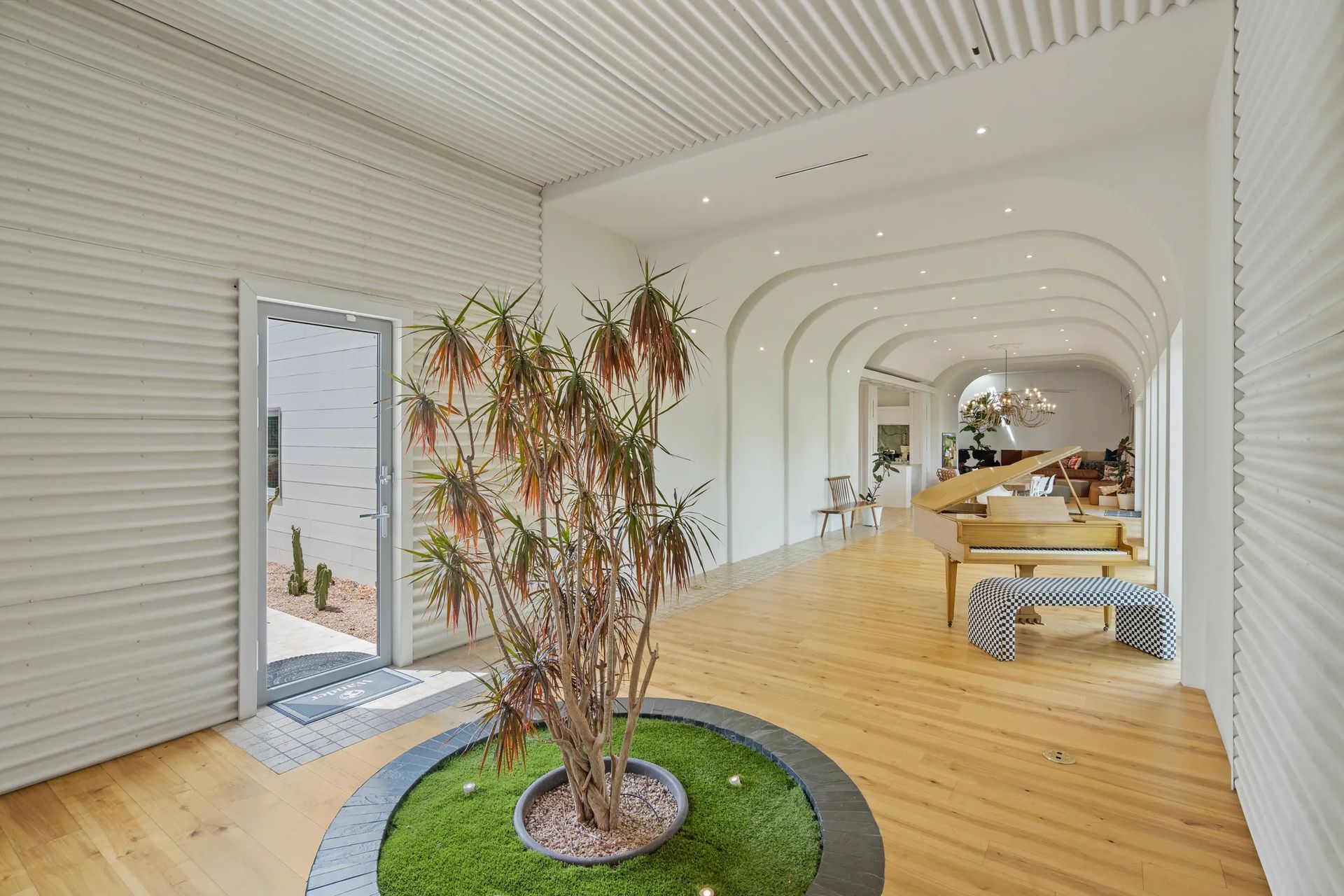 Interior hallway with a plant in the center, light wood floors, white walls, and arched ceilings.
