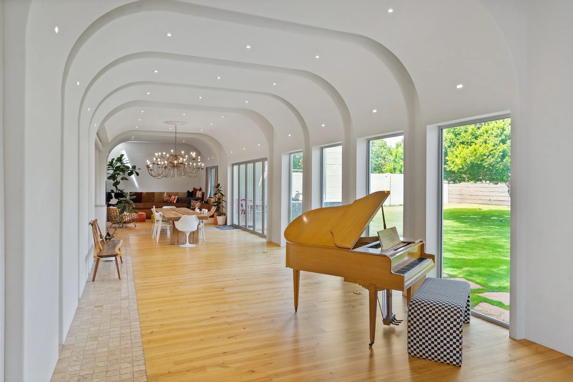 A long, light-filled room with arched ceilings, a grand yellow piano, and large windows overlooking a green yard.