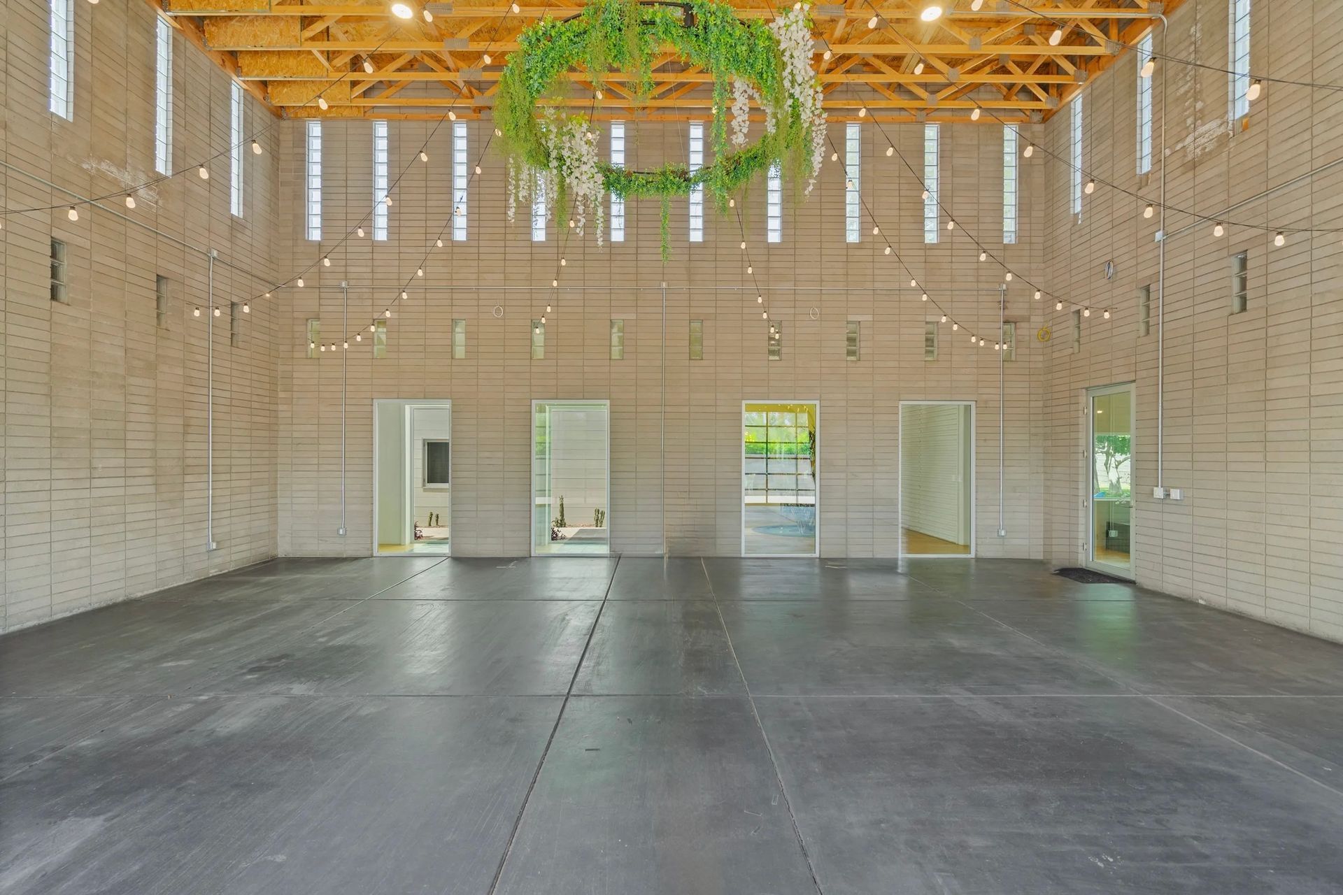 Spacious, modern interior with exposed wood beams, concrete walls, and a large floral wreath. Three open doorways lead to other rooms.
