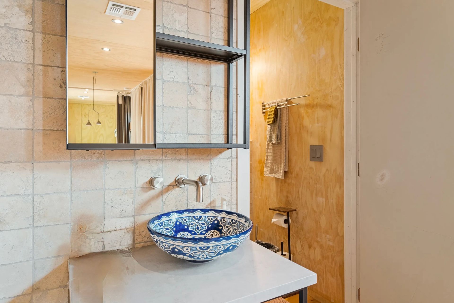 Bathroom with a blue and white patterned sink, mirror, and a neutral-toned wall.