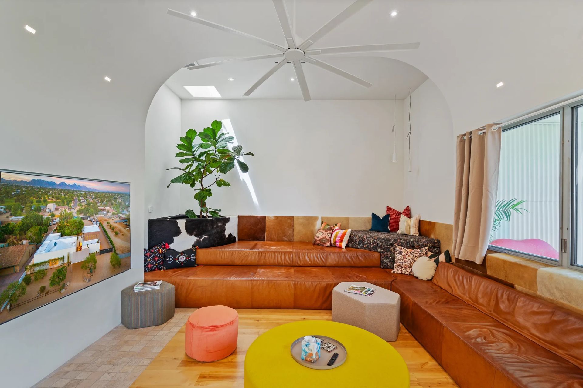 A modern, white-walled living room with built-in, tiered leather seating. A large ceiling fan and plants add to the decor.