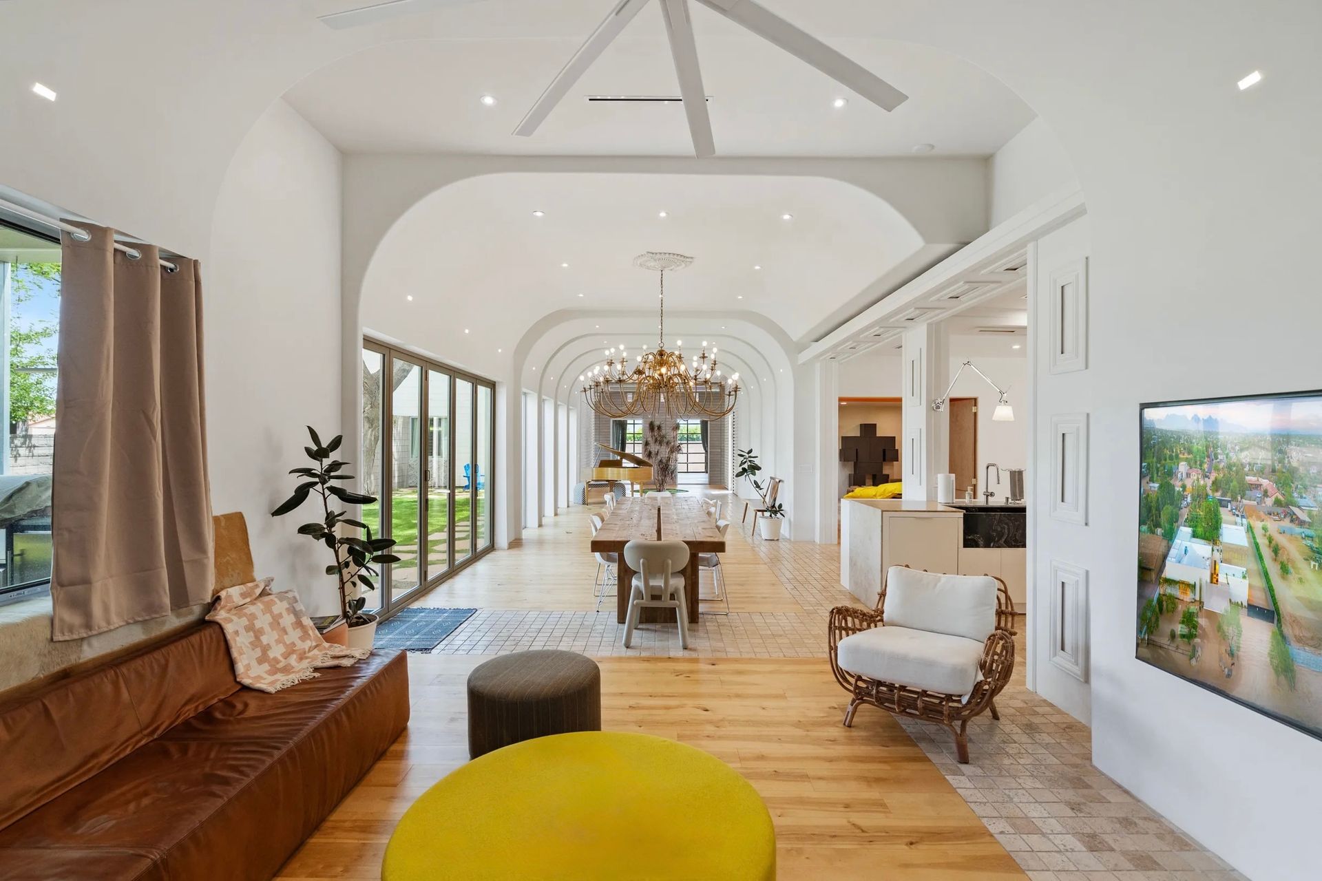 Spacious, bright interior with arched ceilings, wooden floors, and glass doors. Living area with seating, leading to dining and kitchen.