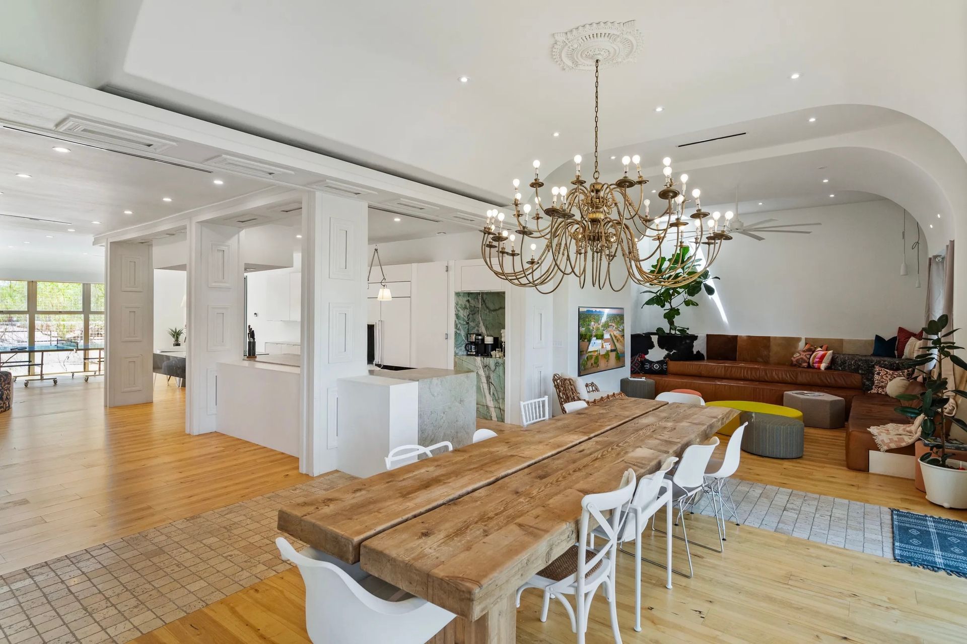 Spacious, modern dining area with long wooden table and chandelier; connects to open kitchen and living room.
