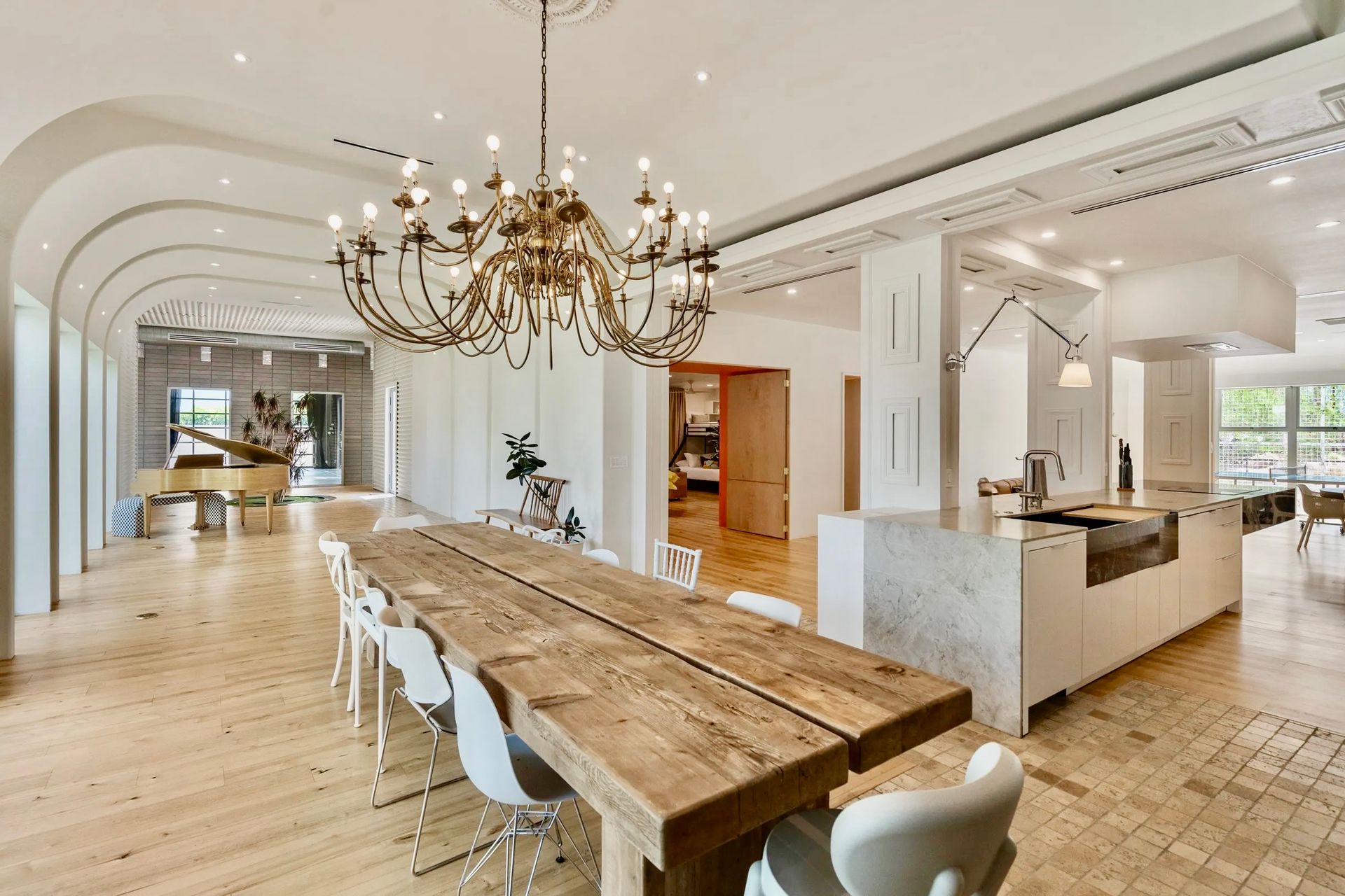 Spacious, bright dining area with a long wooden table, a large chandelier, and an open kitchen.