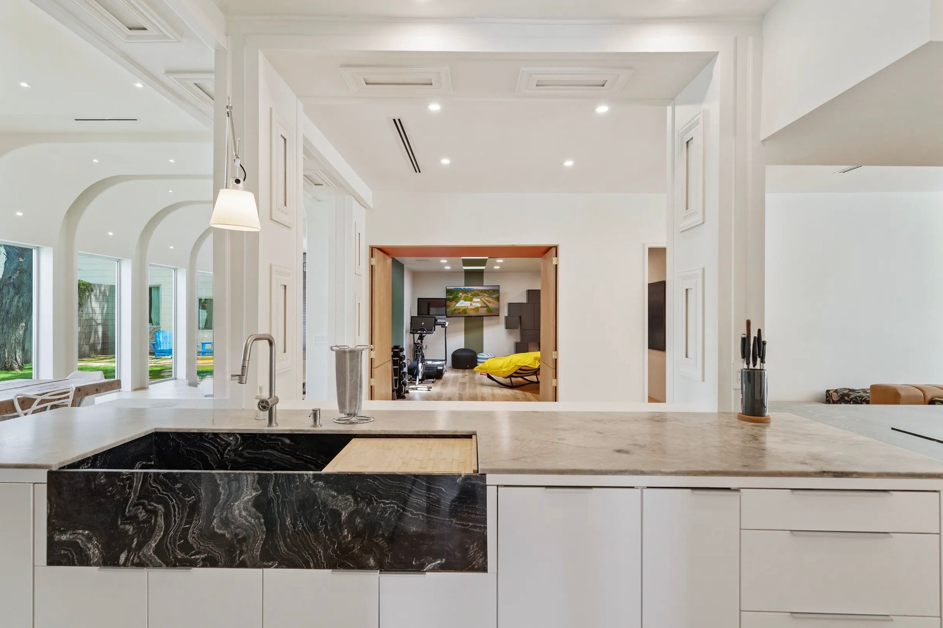 Kitchen with black marble sink, white cabinets, and view into an exercise room with yellow chair.
