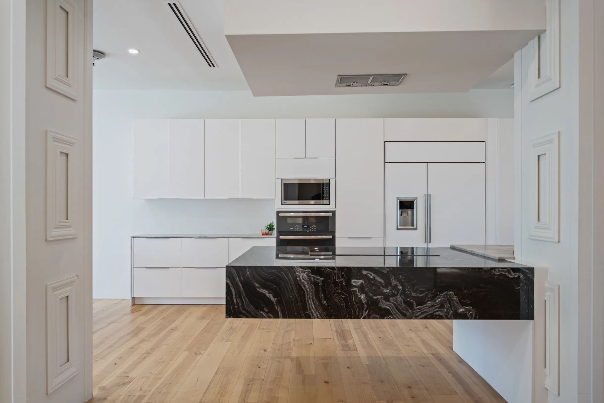 Modern white kitchen with a dark granite island and light wood floors.