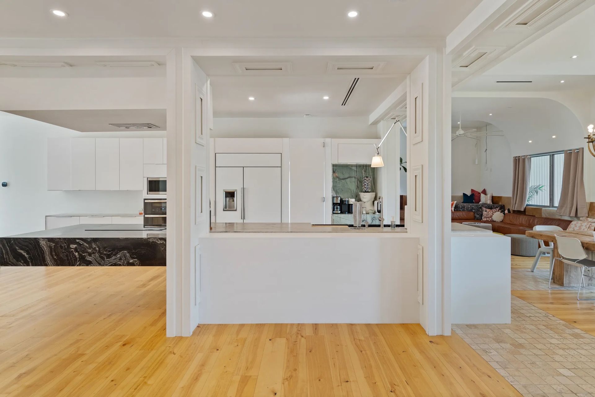Bright kitchen with white cabinetry, marble countertops, and a bar area, visible from an open space with hardwood flooring.