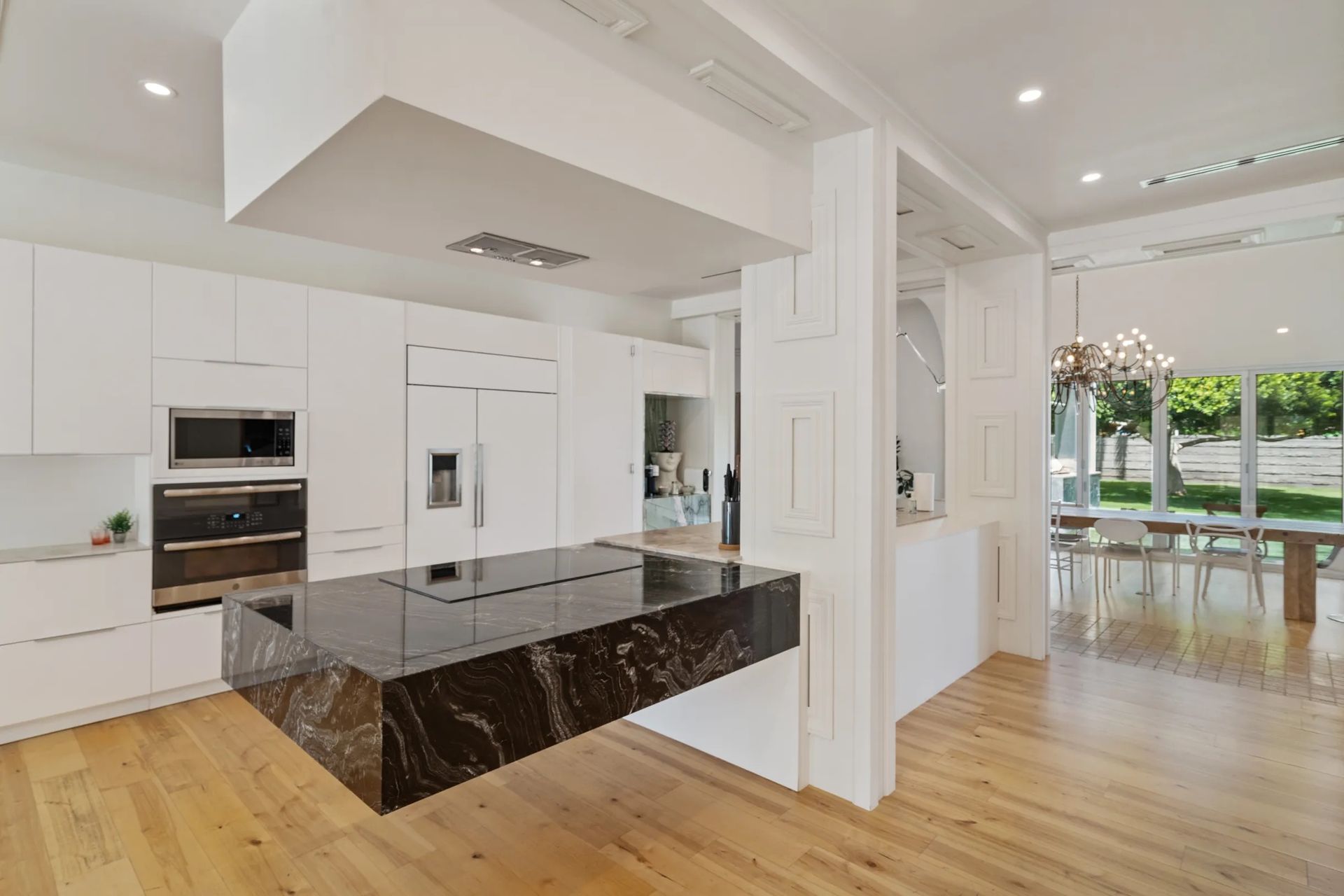 Modern white kitchen with a floating black granite island and light wood floors. Features built-in appliances and opens to a dining area.