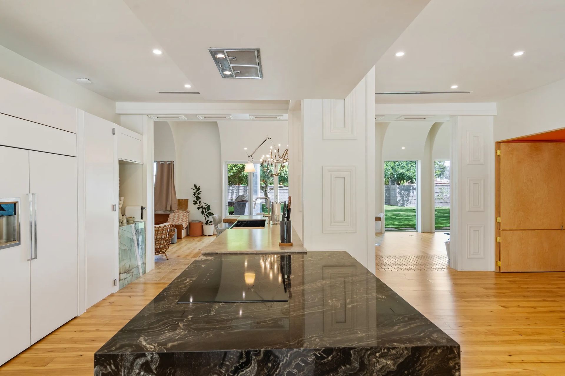 Modern kitchen with a large black granite island, white cabinets, and light wood floors. Arched doorways lead to other rooms.