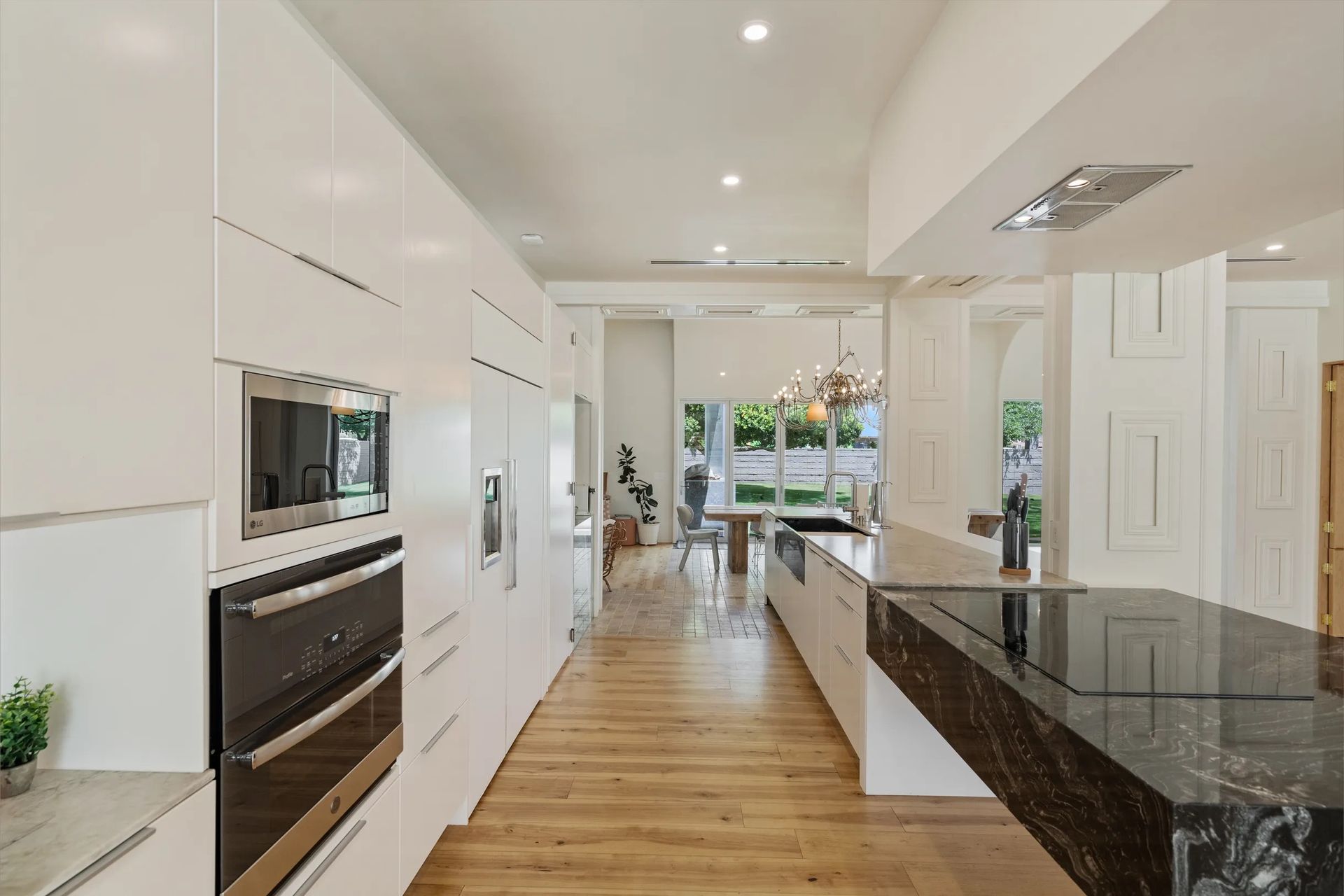 Modern, bright kitchen with white cabinets, black island countertop, and wooden floors.  A long, narrow space with a view of the dining area.