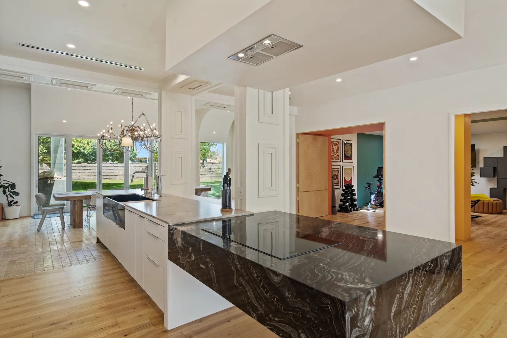 Modern kitchen with white cabinetry, a black granite island, and a view of a dining area and other rooms.