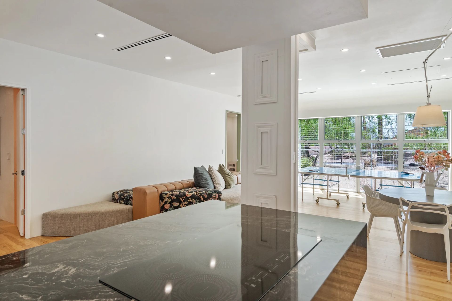 A modern, open-concept living space with a kitchen island in the foreground, a sitting area, and a dining space with a large window.