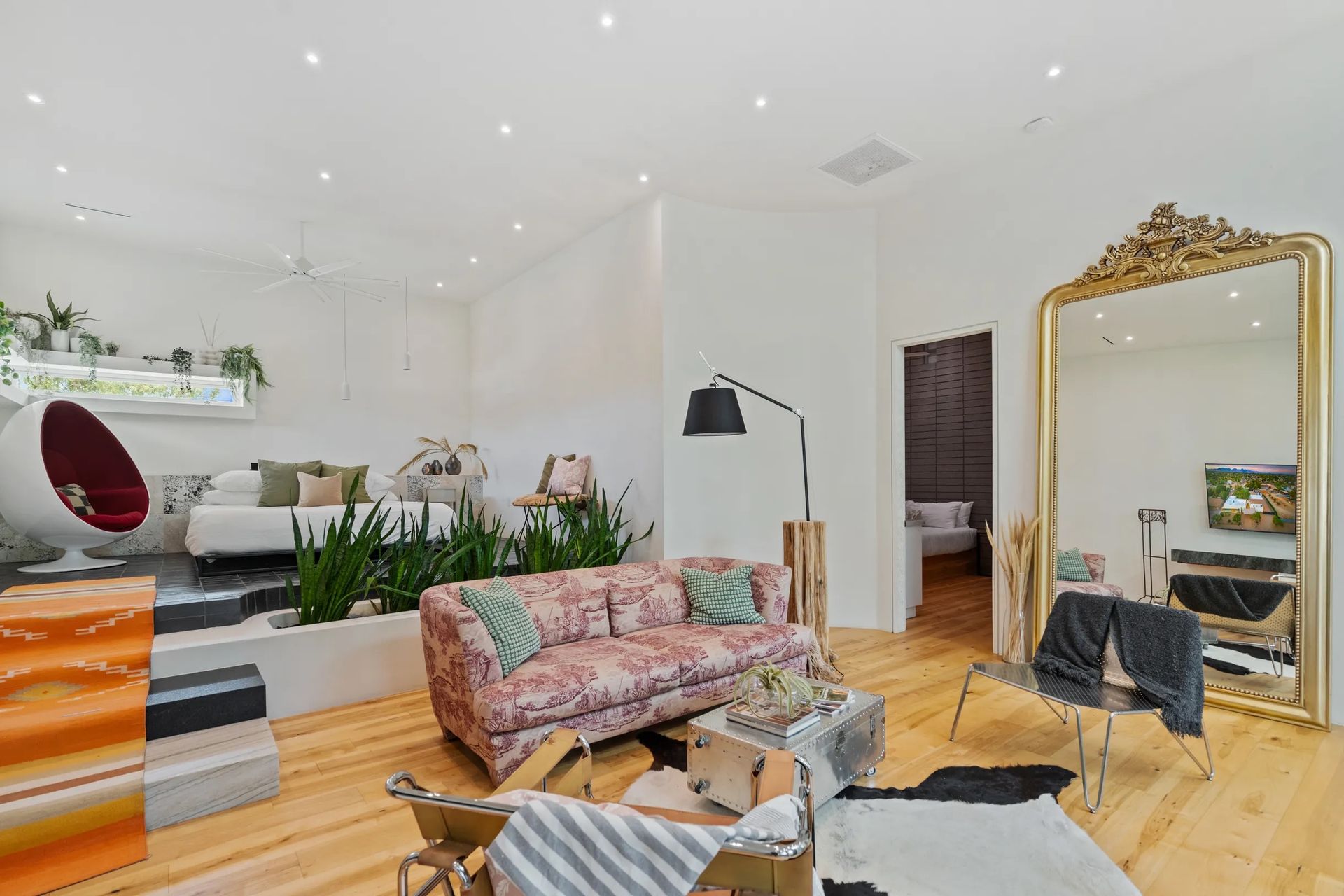 Bright, open room with a pink sofa, large gold mirror, and a seating area with plants.