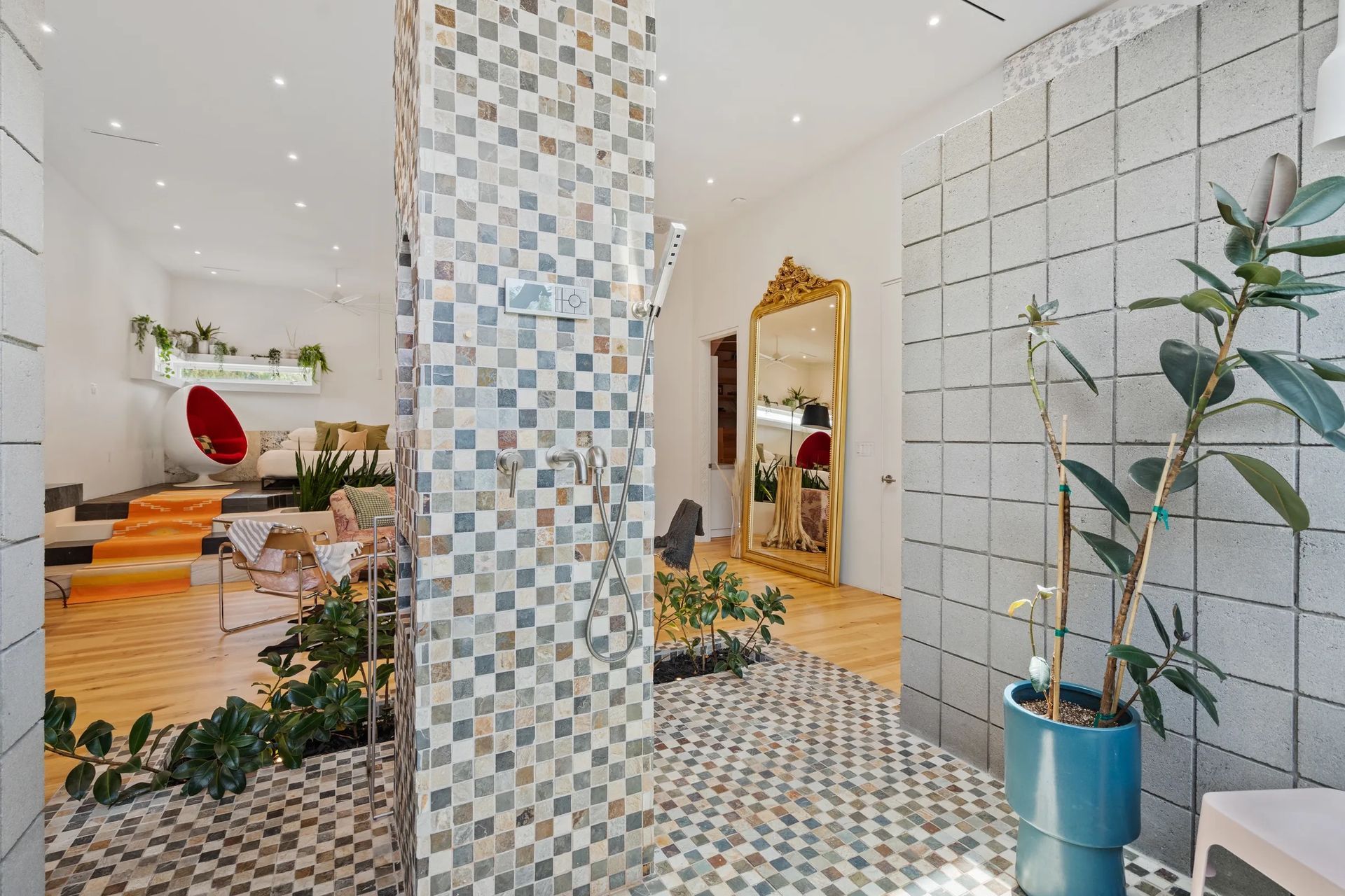 Interior with tiled walls and floors, a large gold mirror, and potted plants. Bright, open space.