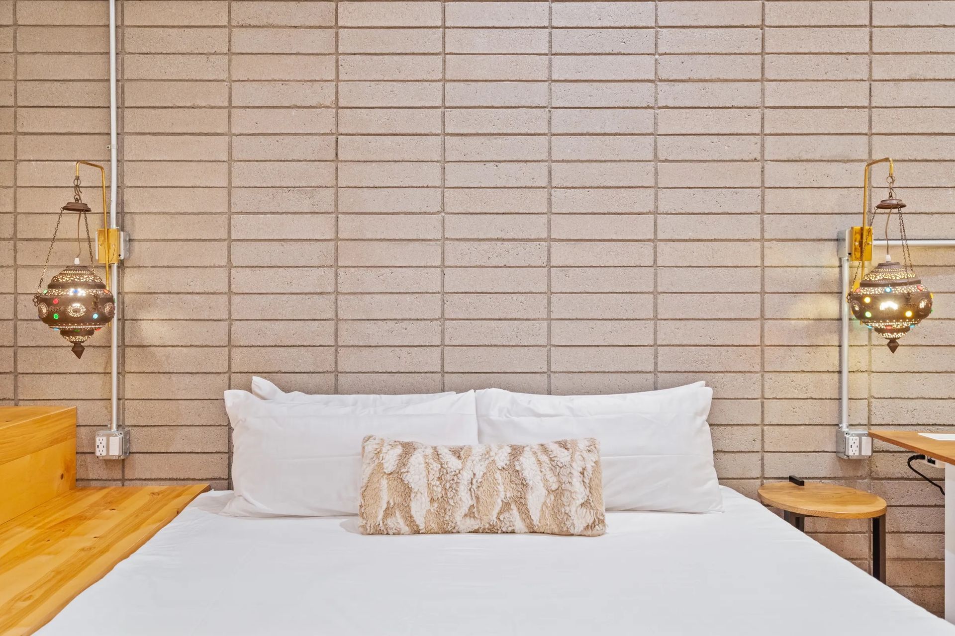 Bedroom with a white-sheeted bed against a textured, gray block wall. Two ornate hanging lamps flank the bed.