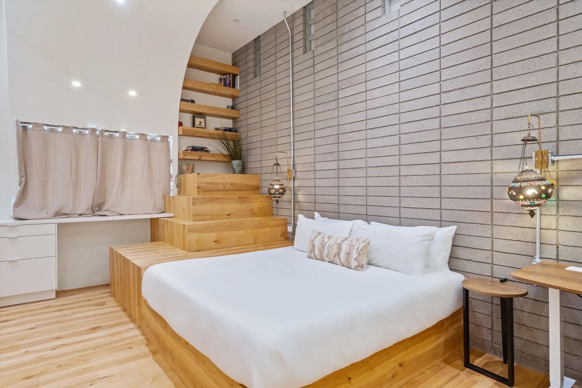 Bedroom with wooden platform bed, steps leading to upper level, and textured gray wall. Includes two bedside tables and window.