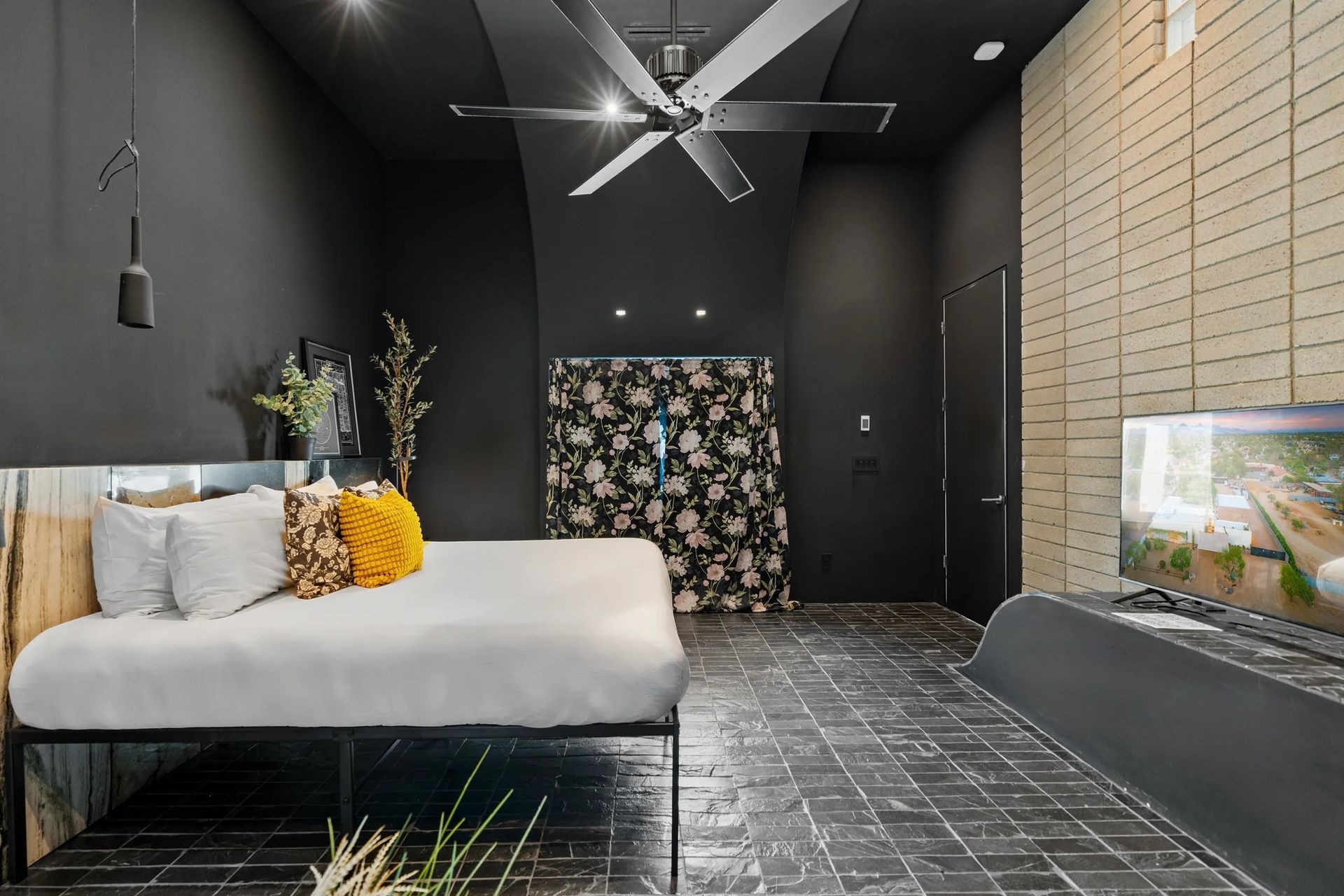 Modern black-walled bedroom with a bed, floral accent wall, tiled floor, and a built-in aquarium.