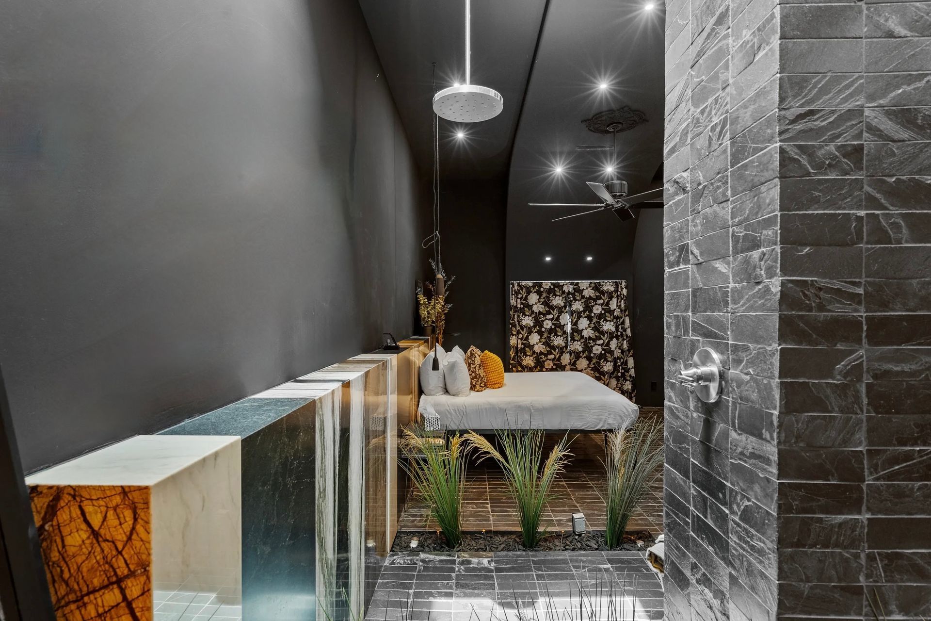 Spa massage room with a massage table, modern decor, and a dark color scheme.  A shower with dark tiled wall on the right.