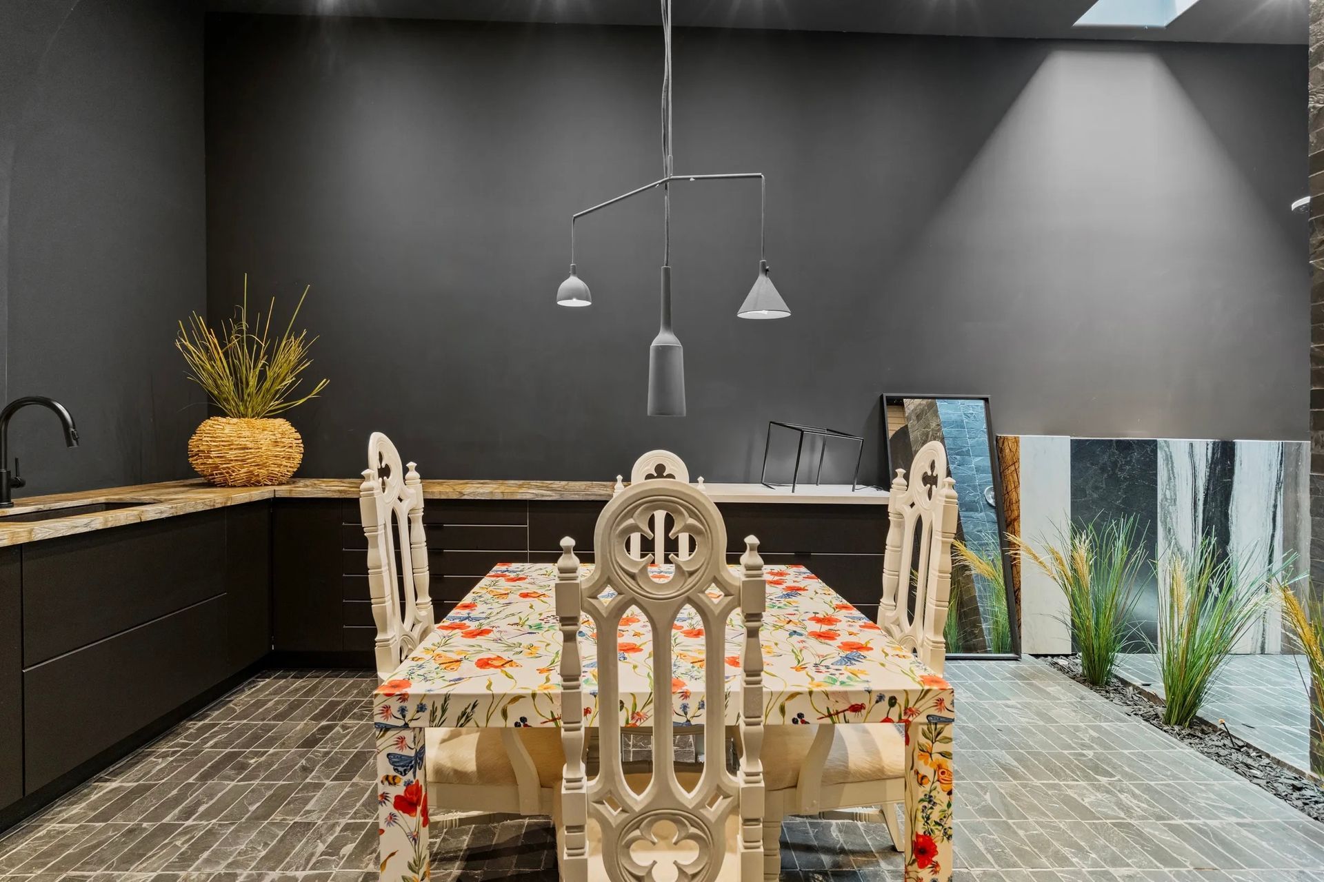 Dining room with dark gray walls, a colorful patterned table, ornate white chairs, and a modern pendant light.