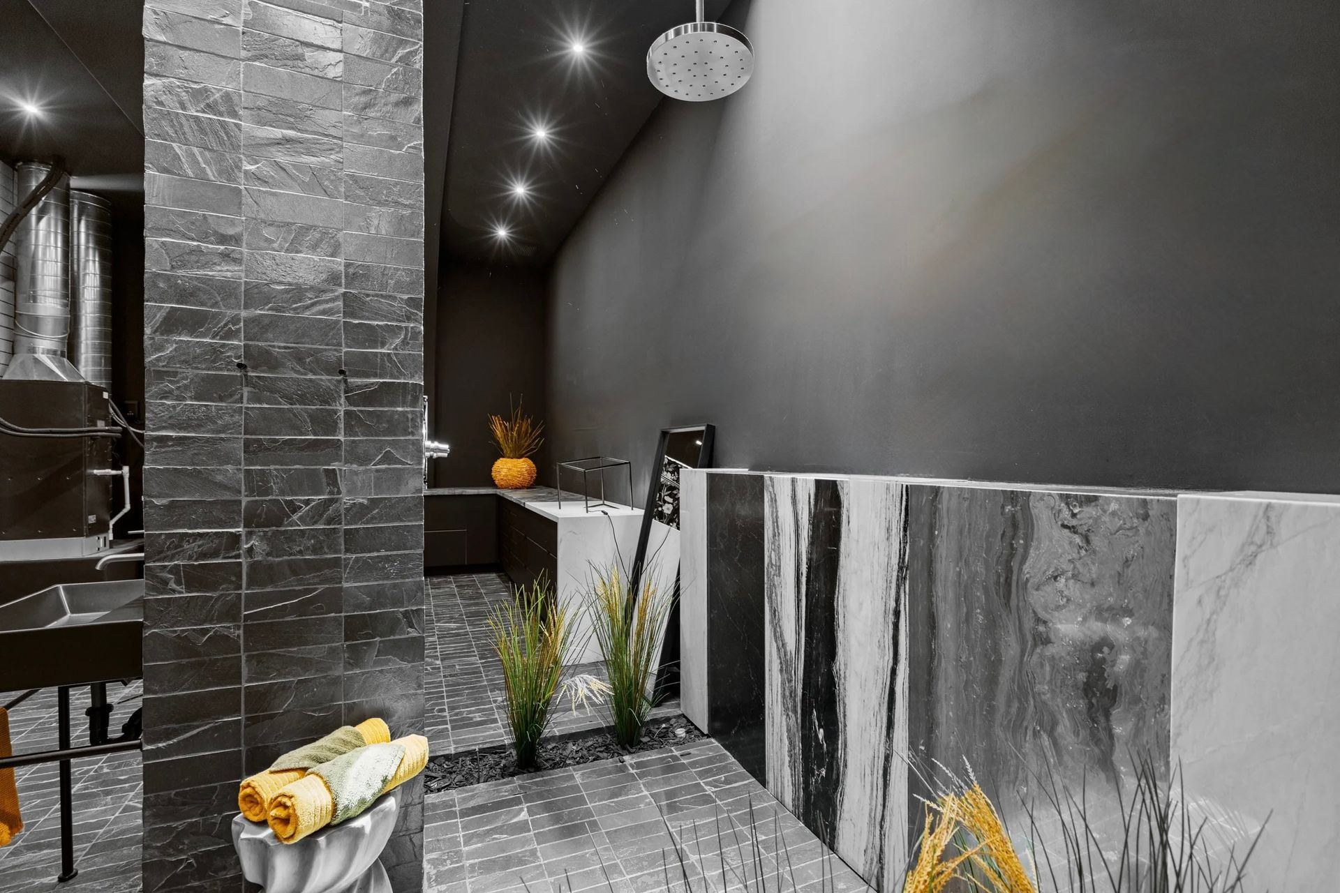 Interior with dark gray stone walls, a counter, and several textured blocks. Sparse plants and a ceiling spotlight are also visible.