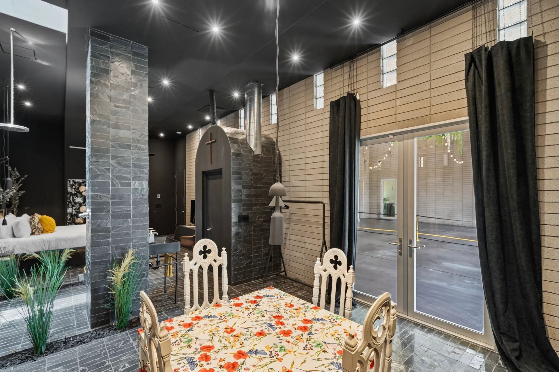 A gothic-style dining room with a dark aesthetic. Features include black walls, ornate chairs, and a large window with a black curtain.