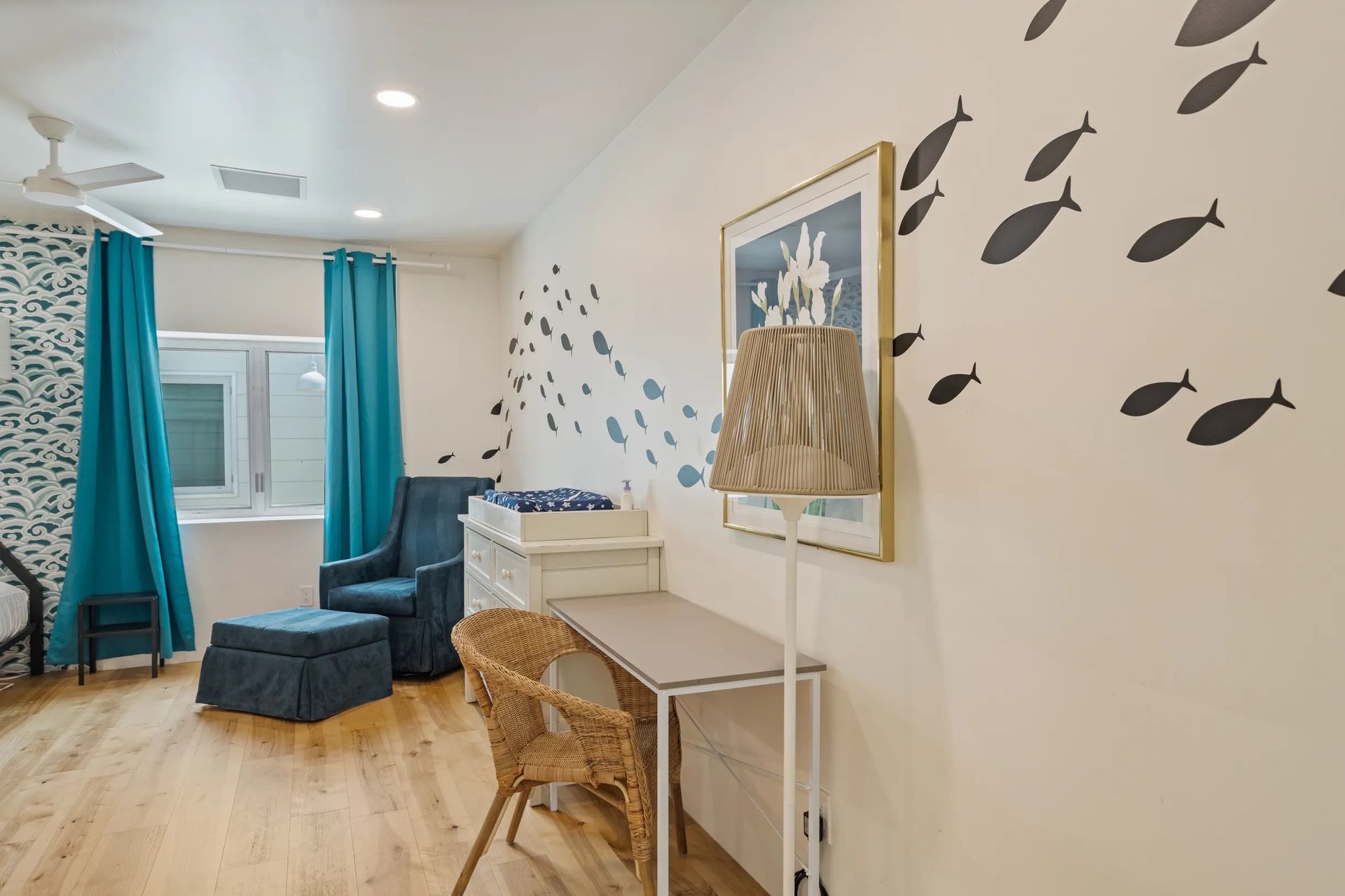Nursery with a teal and white color scheme. A blue armchair, changing table, and fish wall decals decorate the room.